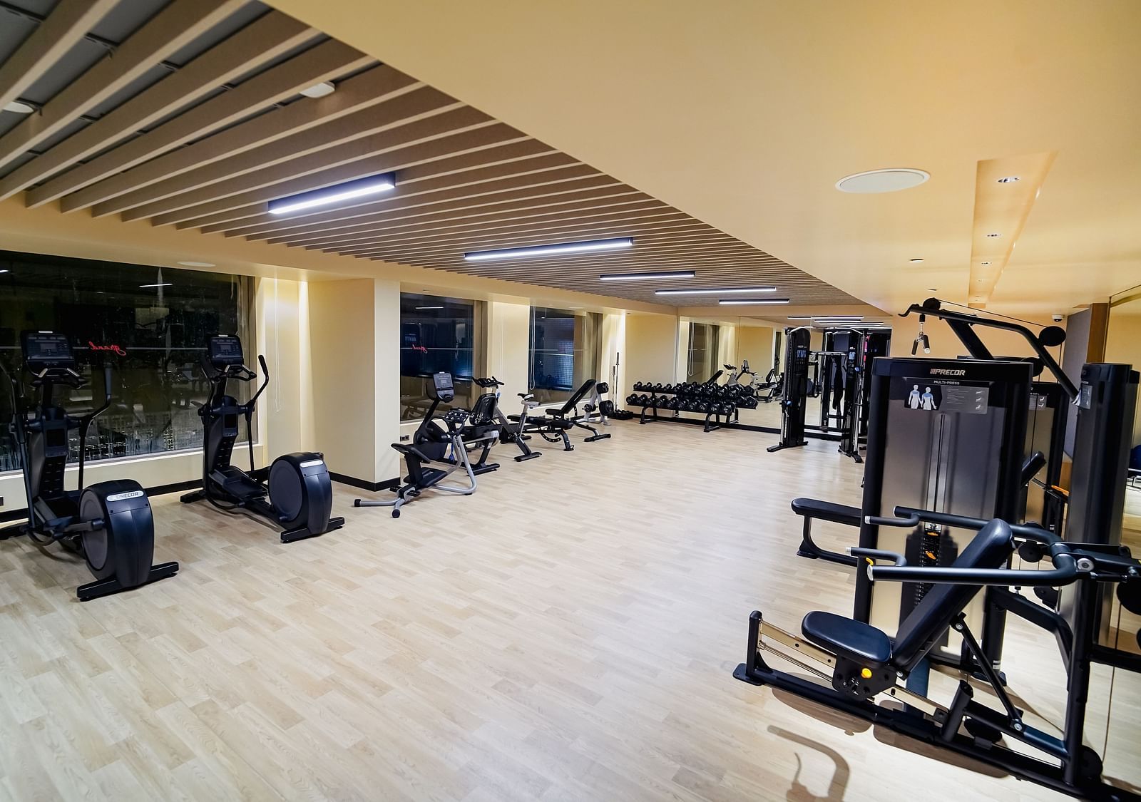 Wide-angle shot of a well-equipped modern gym with various exercise machines and large windows, likely in a residential building - Grand Madurai by GRT Hotels