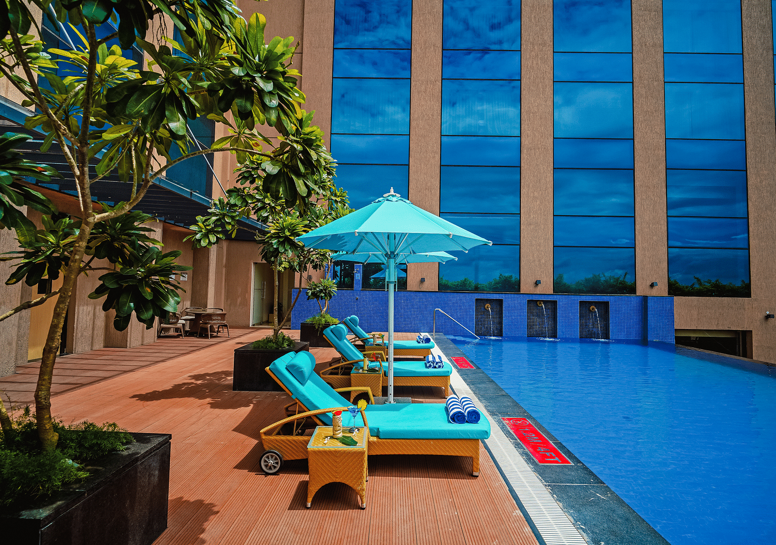 A daytime view of the pool with vibrant blue sun loungers and umbrellas, perfect for a tropical retreat - Grand Madurai by GRT Hotels