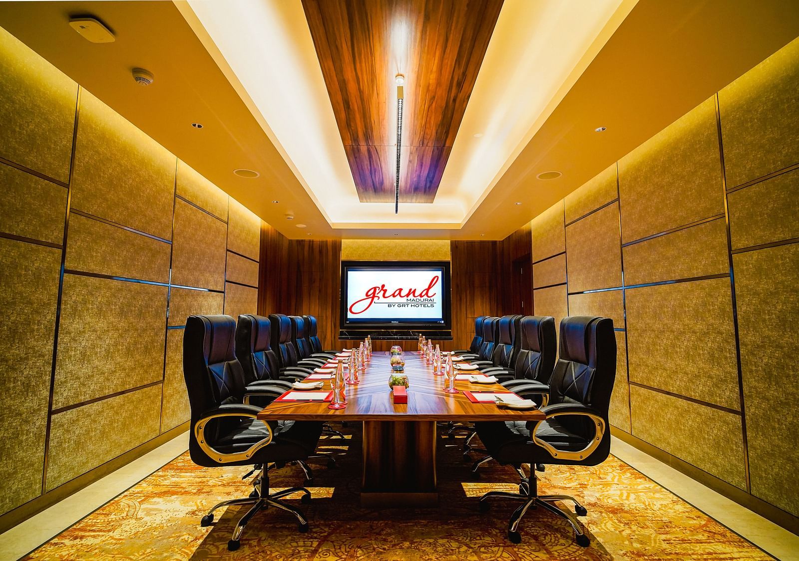 A modern conference room with a large table, executive chairs, and a presentation screen