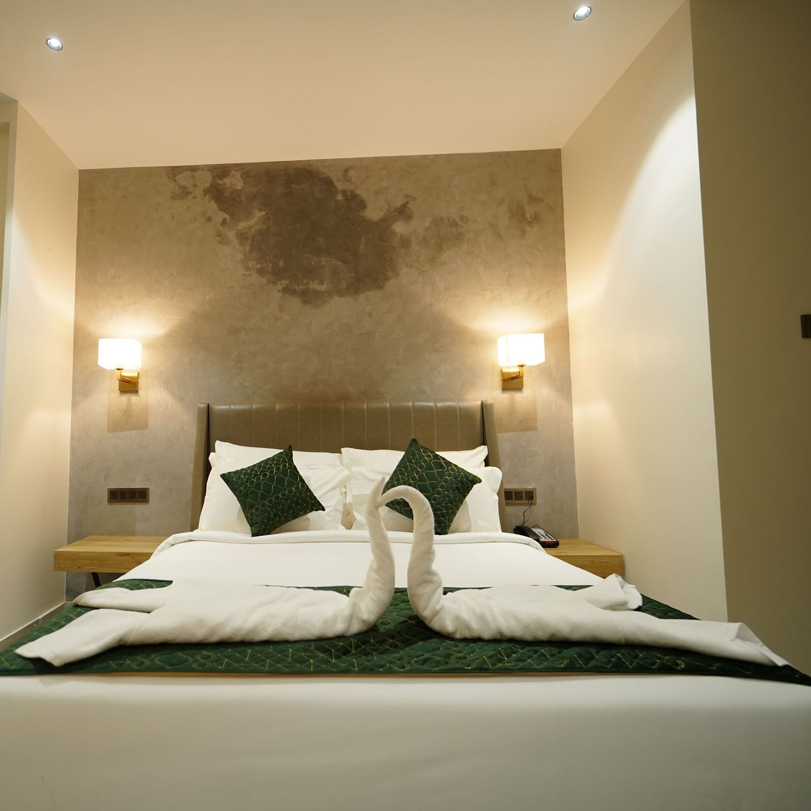 A hotel room has a bed with folded linens, pillows, bedside lamps, a chair, and framed items on the wall - Hotel Park Inn, Nellore.