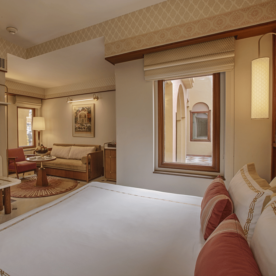 A hotel bedroom with a neat bed, wall-mounted TV, small window, and a seating area with a sofa, chair, and coffee table - Heritage Village Resorts & Spa, Manesar