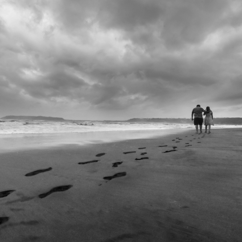 2 people walking on a sandy beach, leaving a trail of footprints behind them under a dramatic sky.