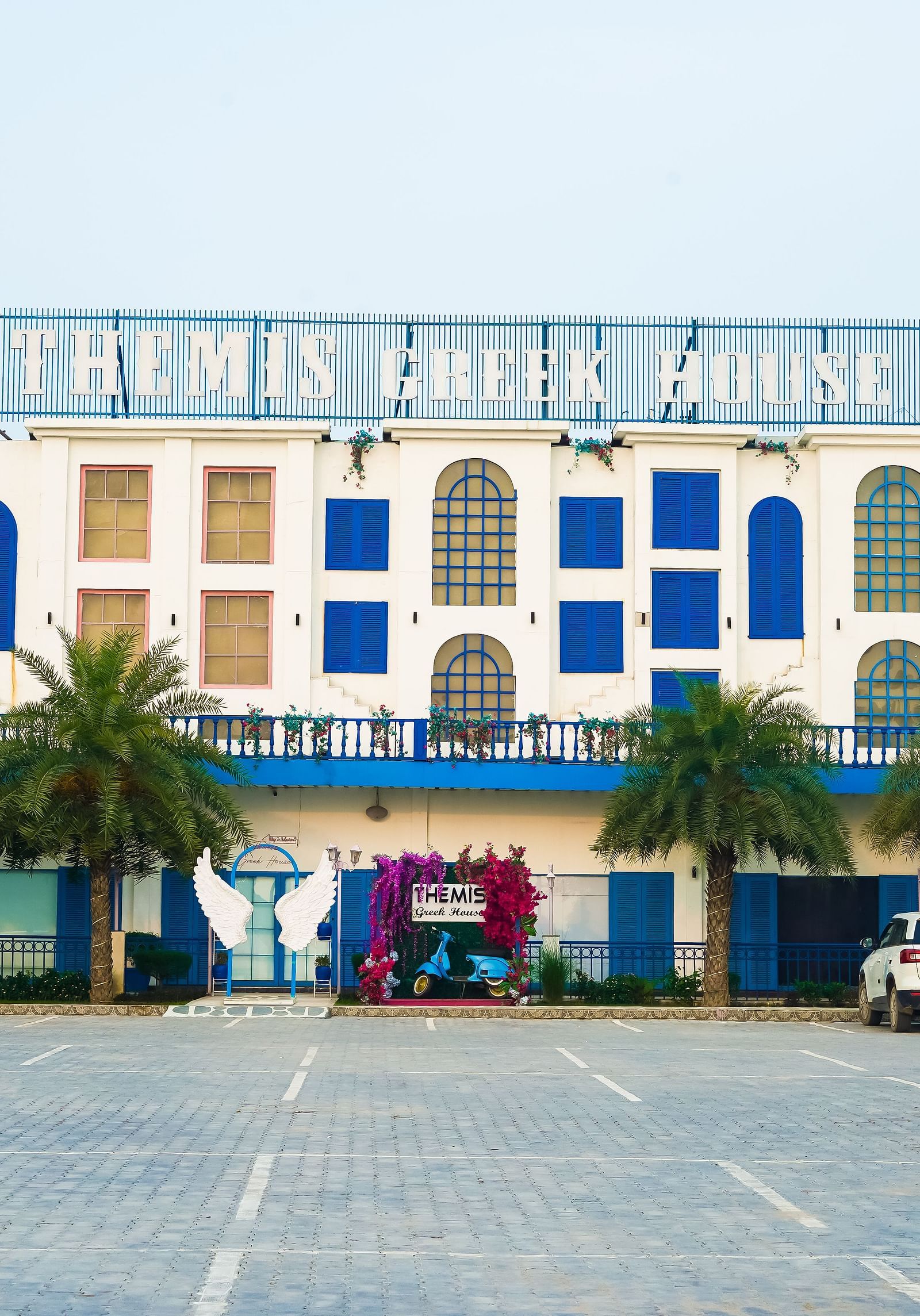 A facade image of Themis Greek House with a parking lot in the front yard 