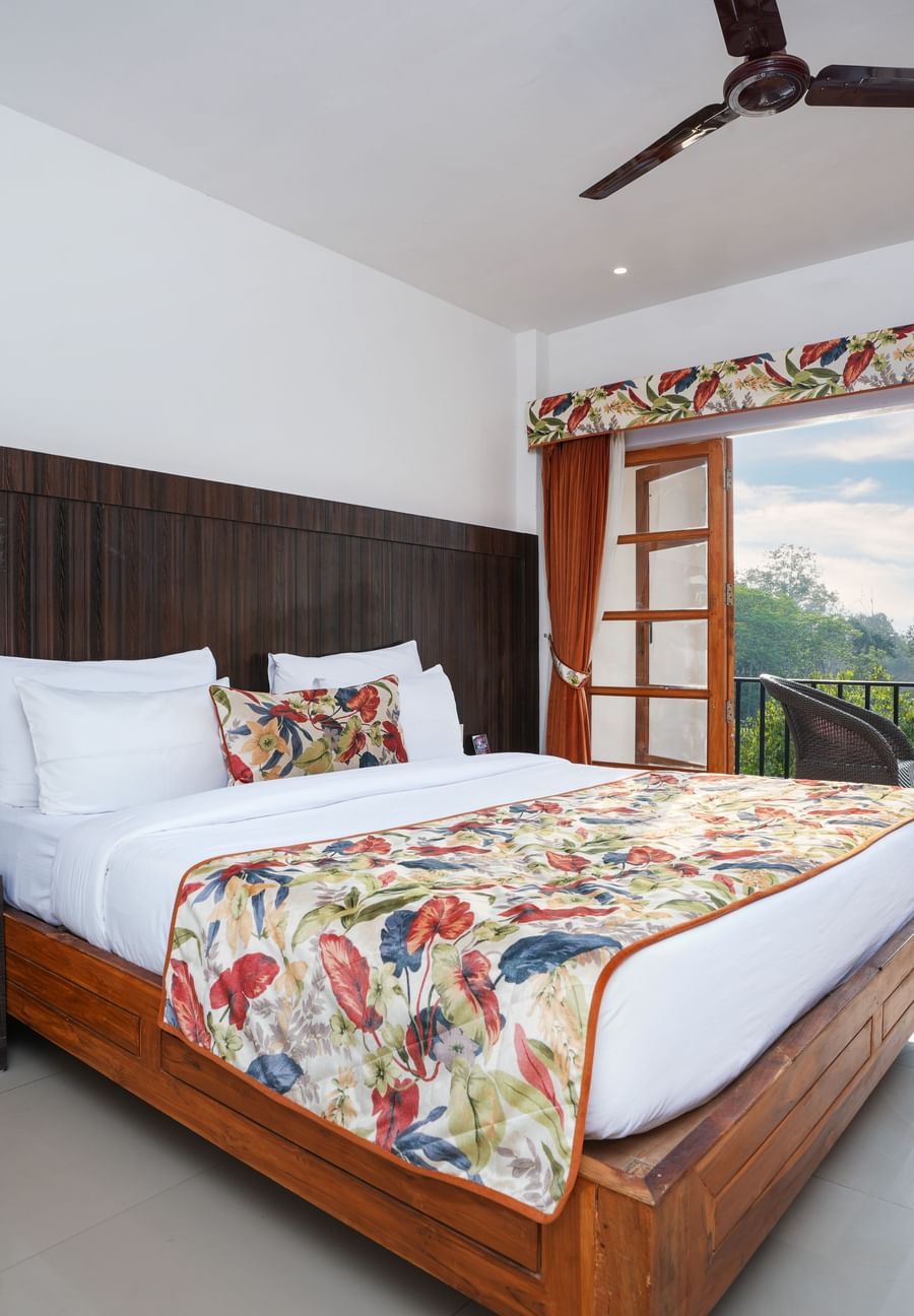 The suite with balcony offers a stunning nature view through large doors that open onto furniture and a glass table at Summit Green Lake Tea Resort & Spa, Kaziranga