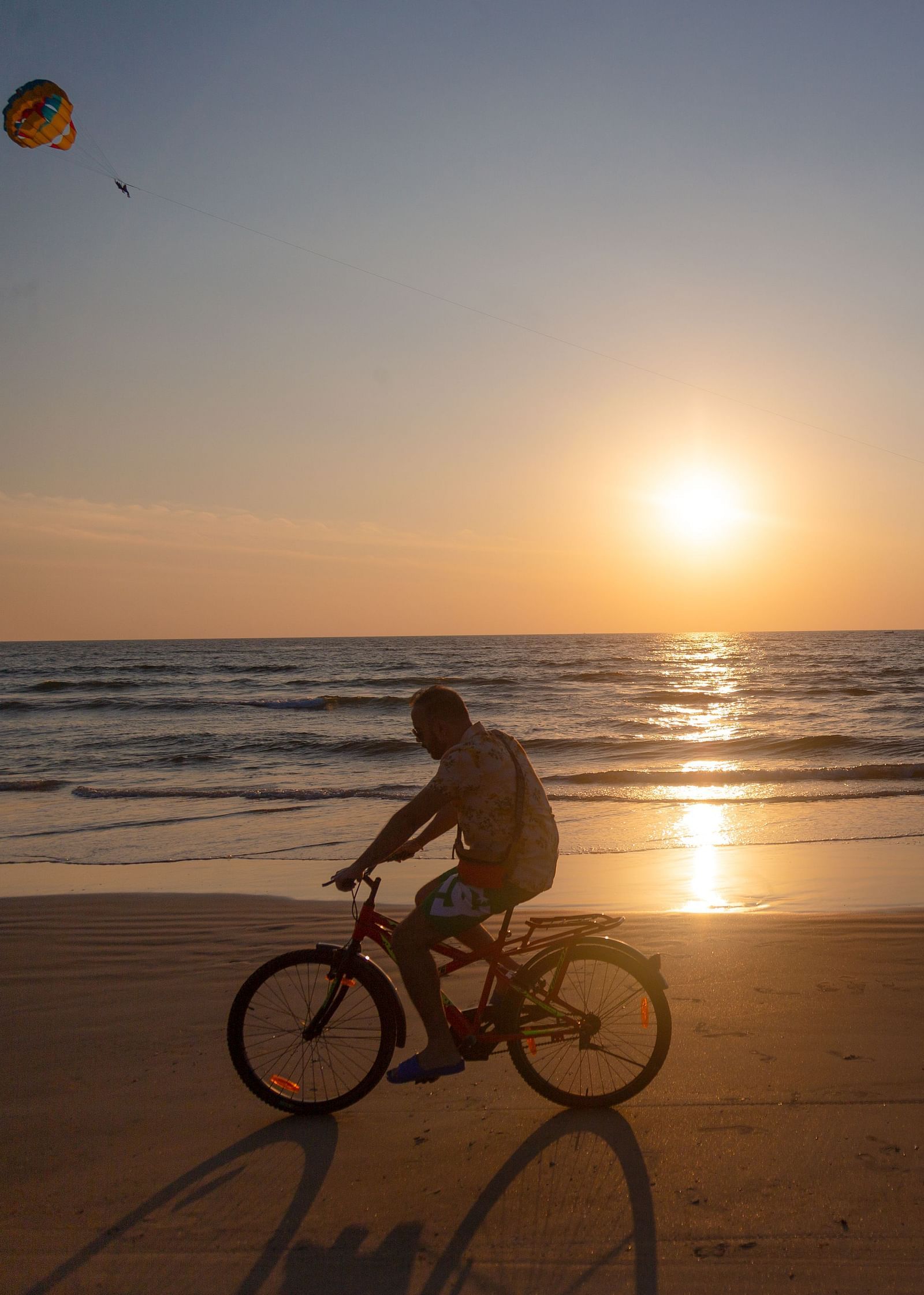 a person cycling on the beach with the sun setting in the background - Caravela Beach Resort Goa