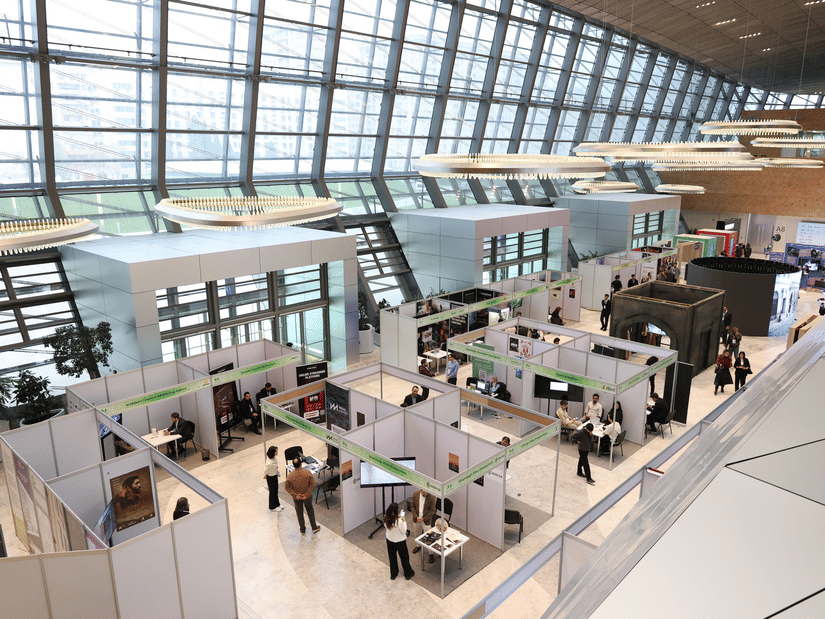 A bustling trade show exhibition inside a modern hall with people networking and exploring booths.