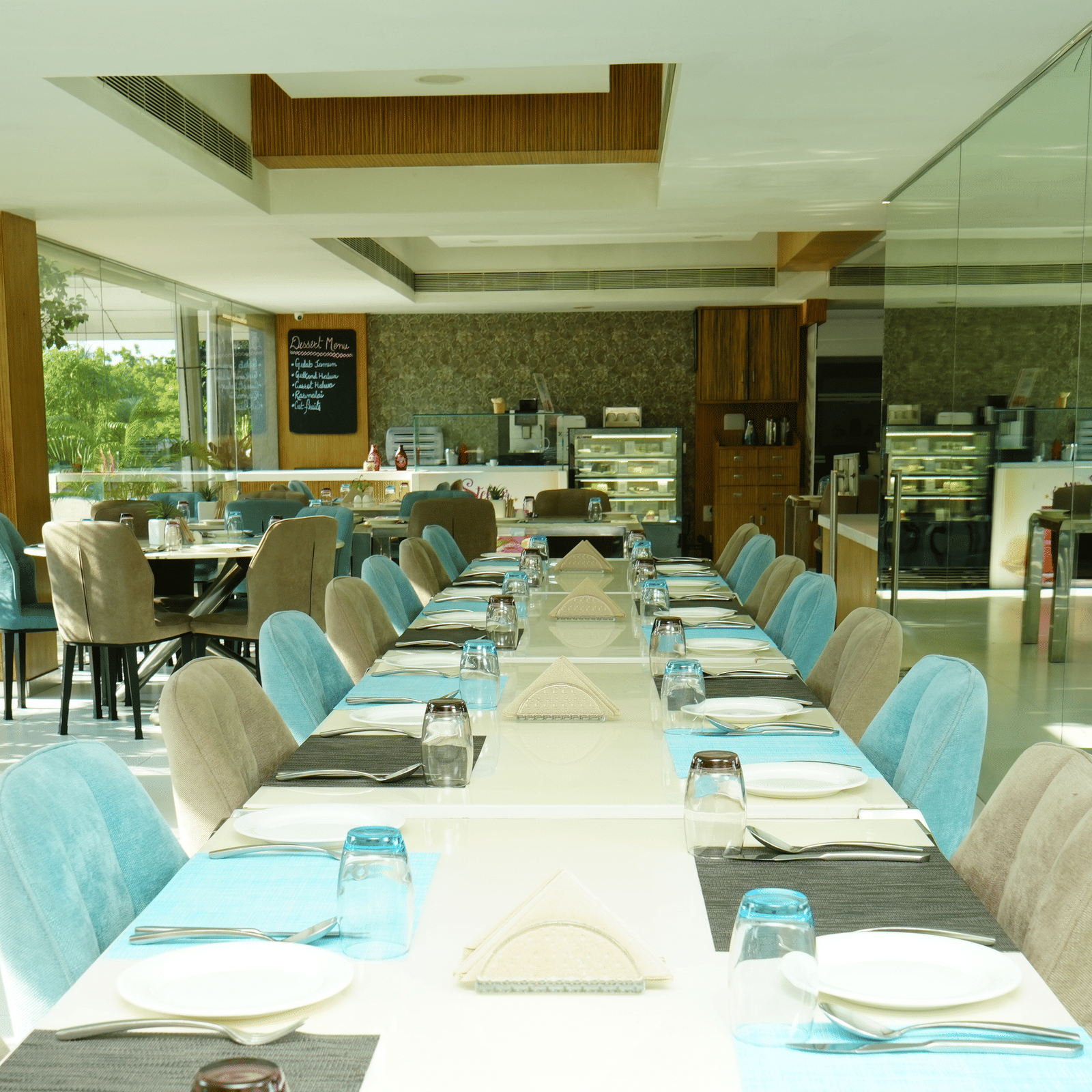 Long indoor dining table setup with turquoise chairs and neatly arranged tableware - Grande Bay Resort & Spa, Mamallapuram
