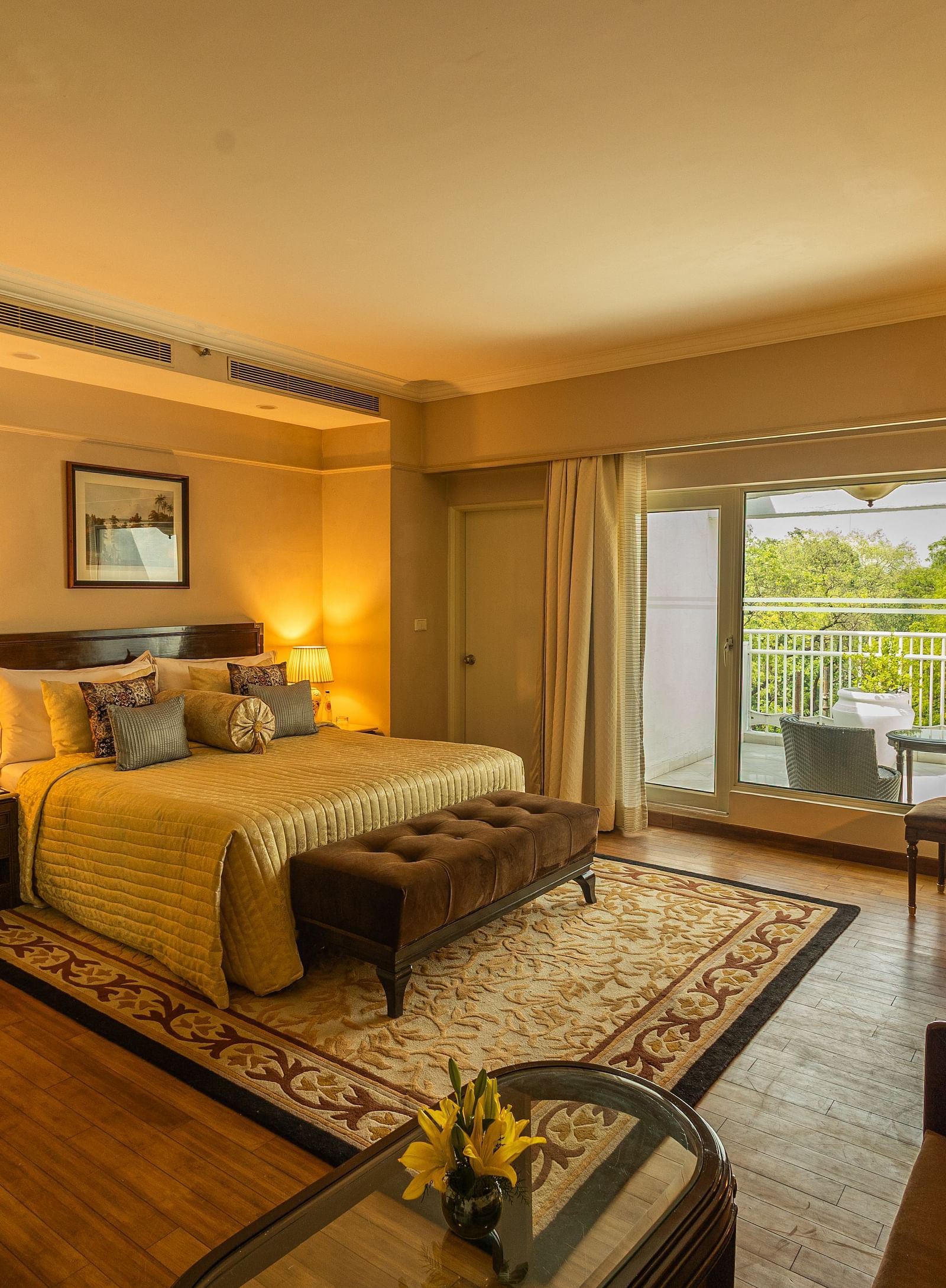 Luxury King Bed Room with Balcony at The Claridges New Delhi, featuring a cosy bed, a framed artwork on the wall, and a glass door to the balcony