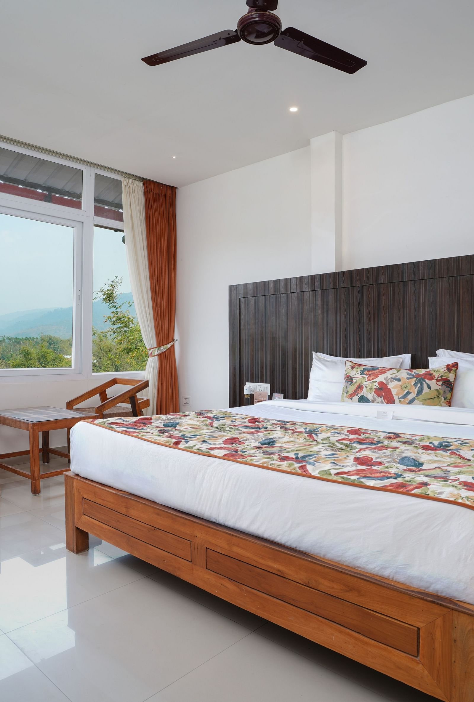 Deluxe room featuring large windows with a nature view, a spacious bed, air conditioning, wooden storage units, and a television at Summit Green Lake Tea Resort & Spa, Kaziranga4