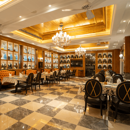 An elegant, formal dining room or restaurant with ornate chandeliers, dark wooden paneling, and a stylish black and white diamond-patterned floor.