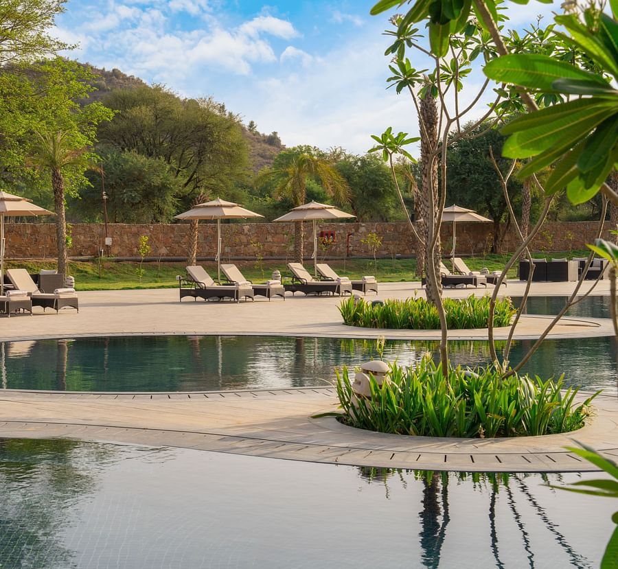 Swimming pool at Ananta Spa and Resort, Ajabgarh with sun-lounger and tress surrounding it.