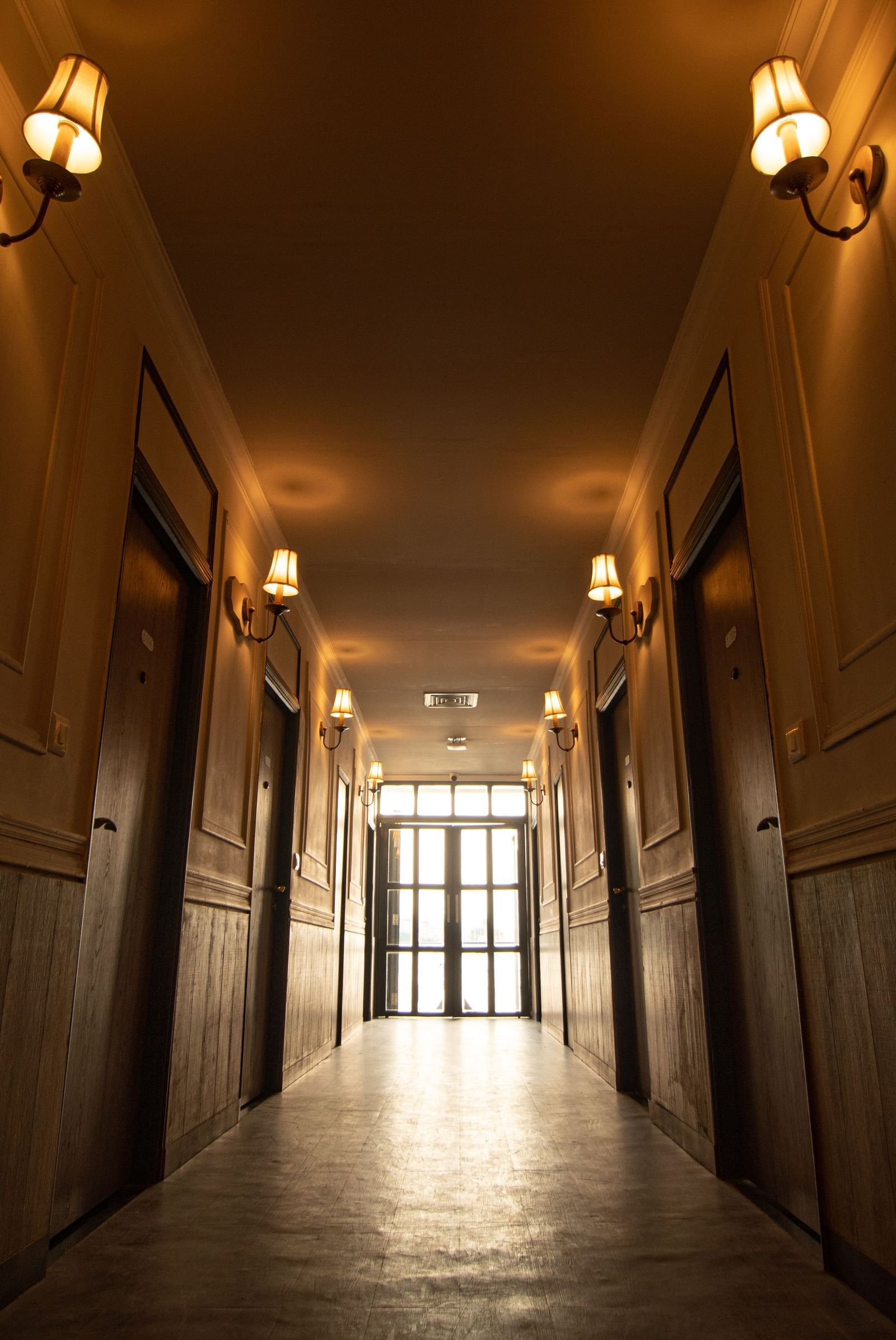 A long and empty hallway at Polo Floatel Kolkata with warm lighting and wooden panelling on the walls.