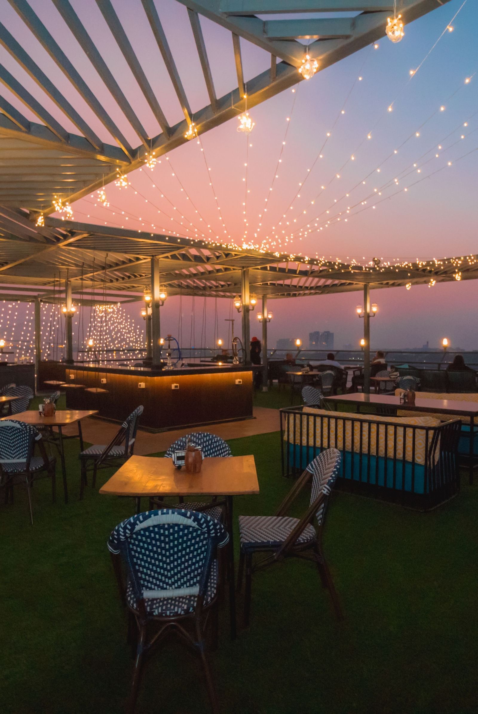 A nighttime view of the outdoor rooftop dining area at Polo Floatel Kolkata. The space is lit by string lights, with various tables and chairs set up under a covered patio. 