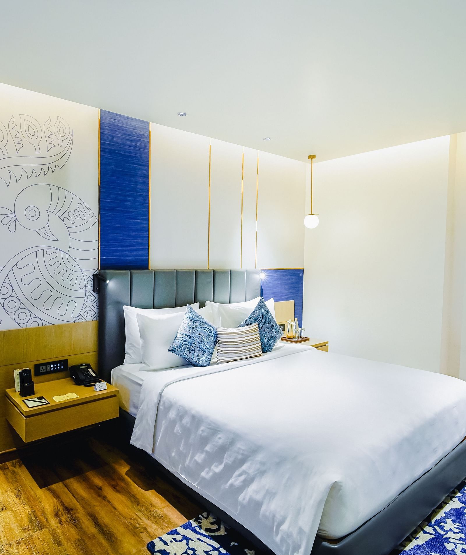 An image of our Deluxe Suite in Madurai with a peacock wall paper, a large bed, a night stand and a blue couch