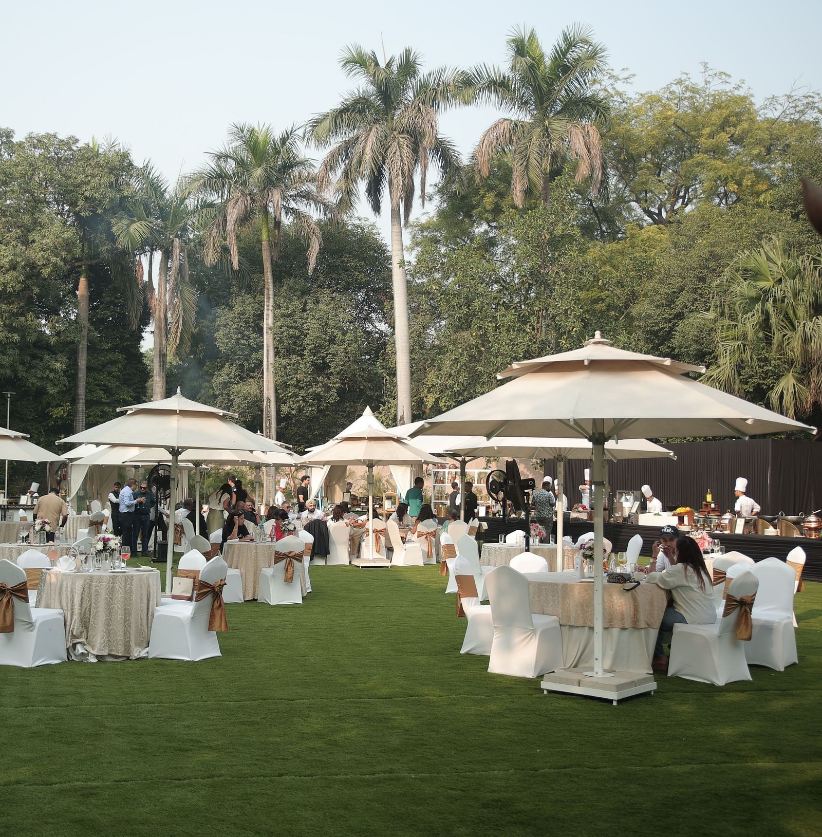 Image of the spacious garden at The Claridges New Delhi, featuring an open area with a clear sky, surrounded by large trees