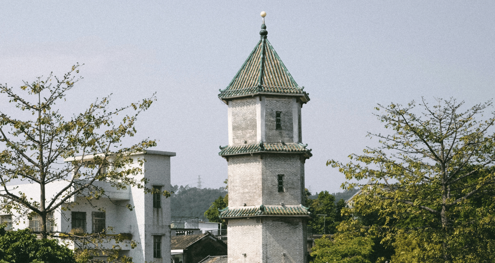 A close-up of a white, multi-level tower structure with a green dome against a pale sky.