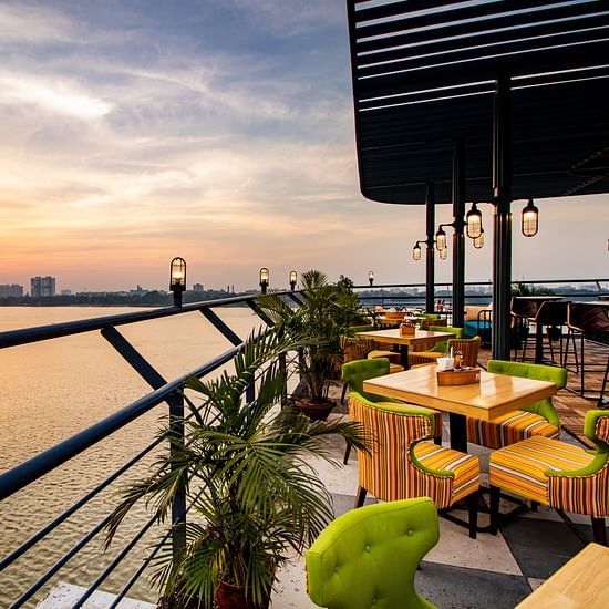 A scenic rooftop restaurant with colorful chairs, wooden tables, and a view of the sunset over a river. - Polo Floatel