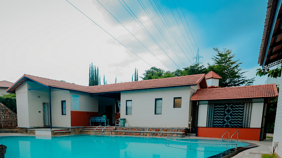 A uniquely shaped swimming pool at Nirantara Resort & Spa, Bengaluru, surrounded by plants and buildings.
