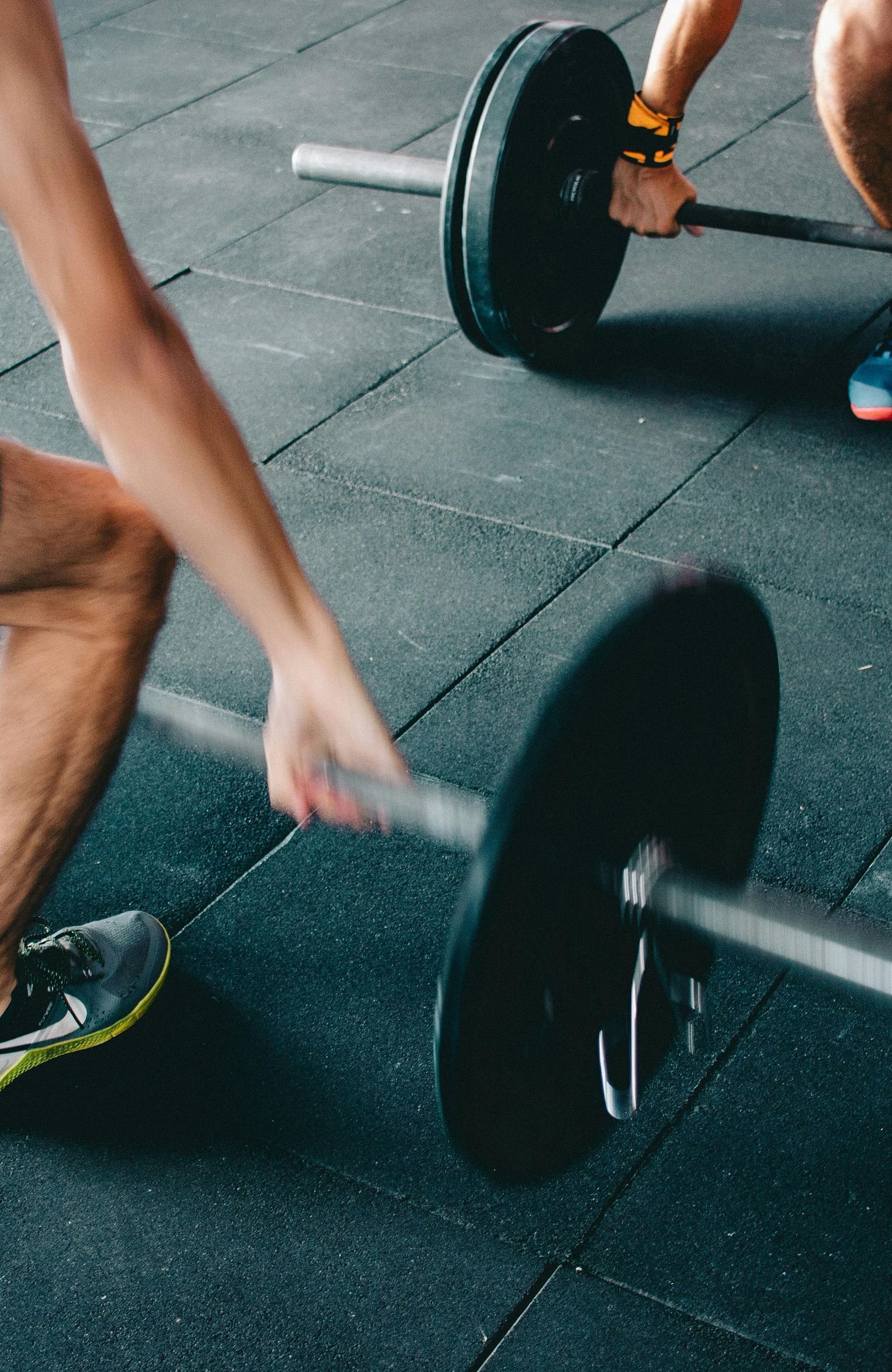 Two men are shown in a gym setting, lifting barbells with weights.