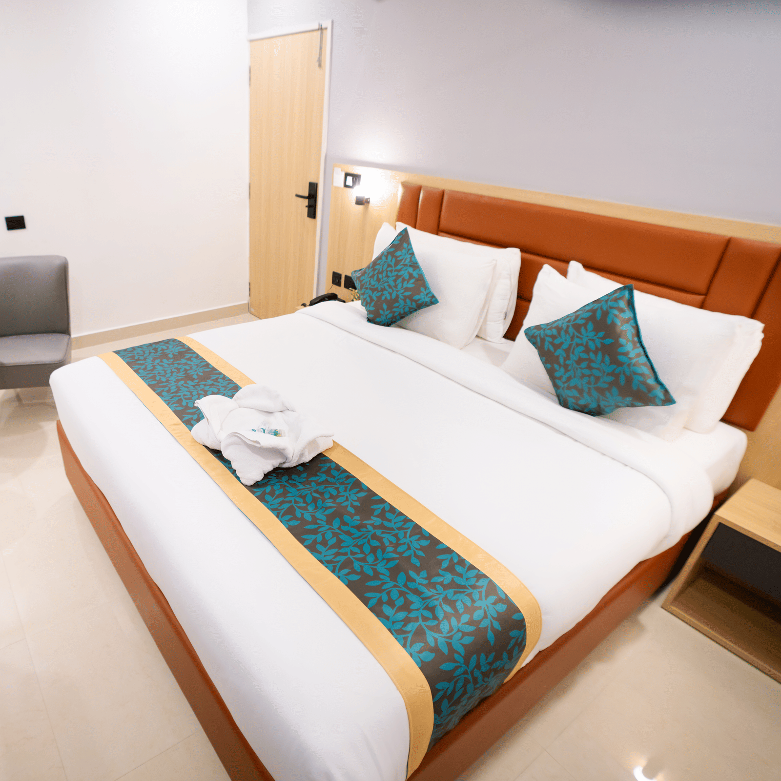 View of a spacious room with a large bed with a headboard, bedside tables on both sides, and a seating area to the side at Sunrise Business Hotel, Hyderabad.