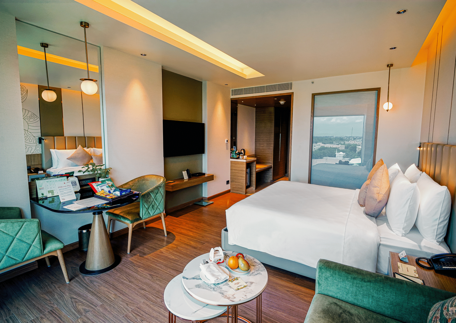 A stylish and well-lit hotel room featuring a cosy bed, elegant seating, and a scenic city view through a large window - Grand Madurai by GRT Hotels