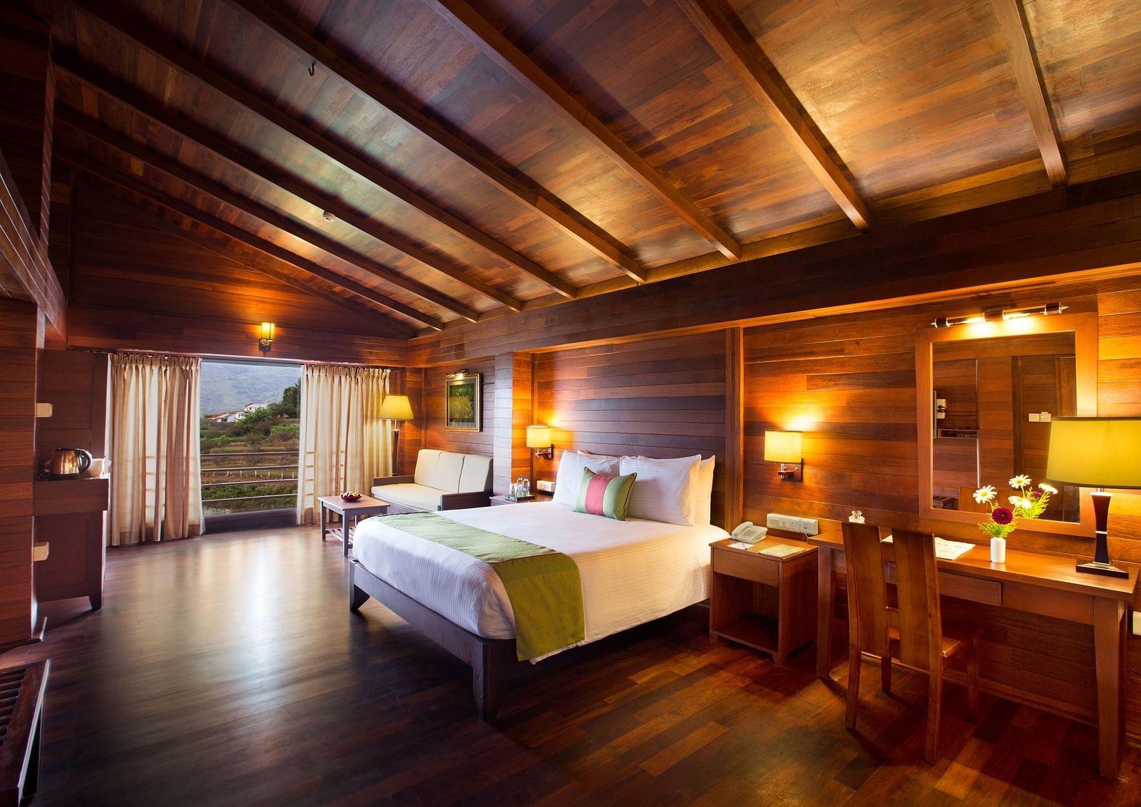An image of Timber Charlet room with a king size bed, bed side table, lamps, a dressing table, chair, and other decorative items - GReaT Trails Kodaikanal By GRT Hotels