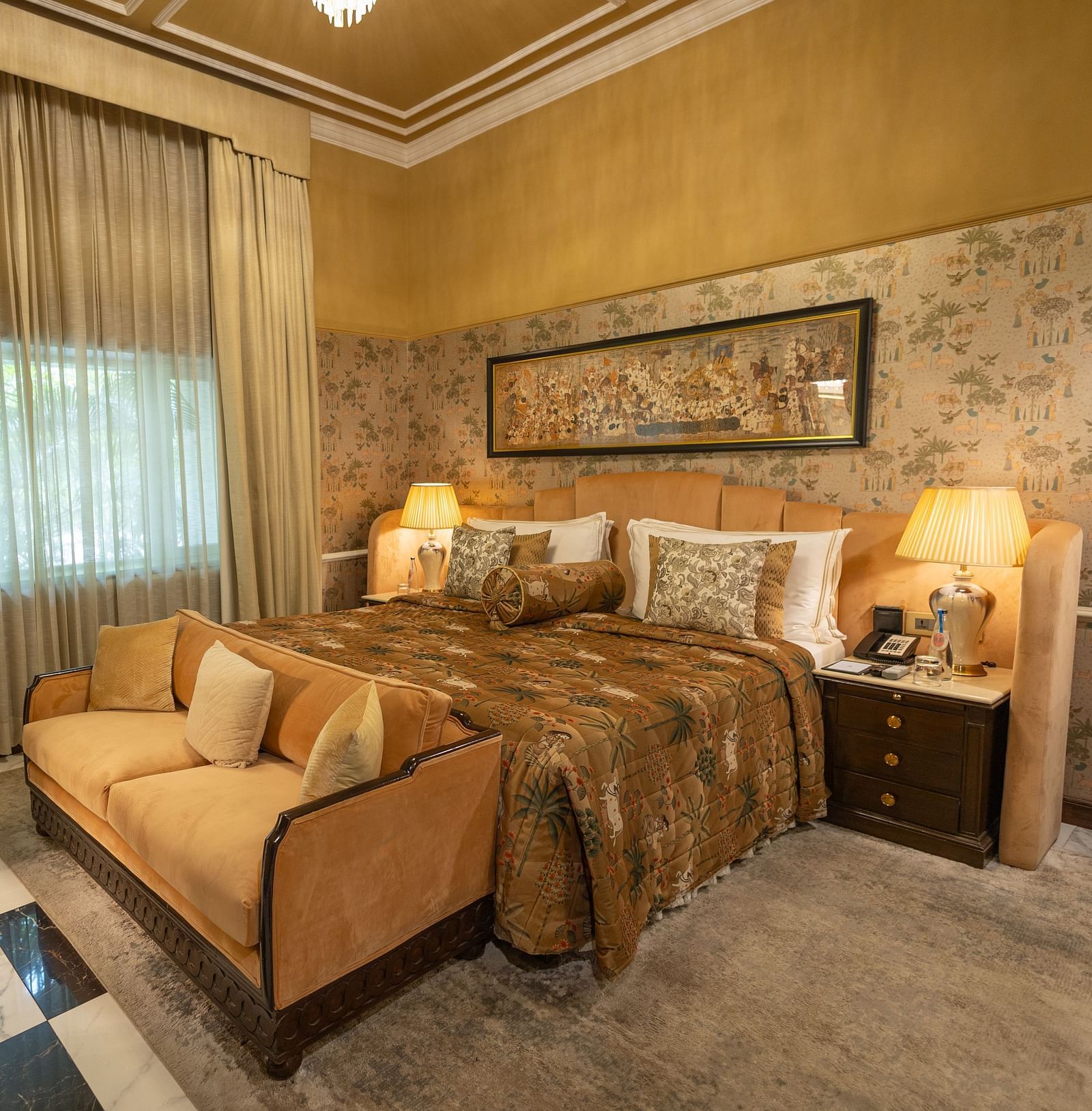 Executive Suite at The Claridges New Delhi, featuring a cosy king sized bed, a sofa placed in front, and a bedside lamp