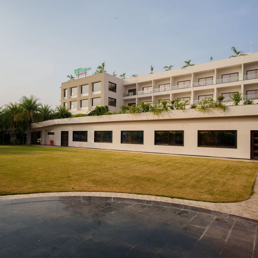 Exterior view of the low-rise hotel building adjacent to a large, well-maintained green lawn area at Arawali Ananta Elite, Jaipur.