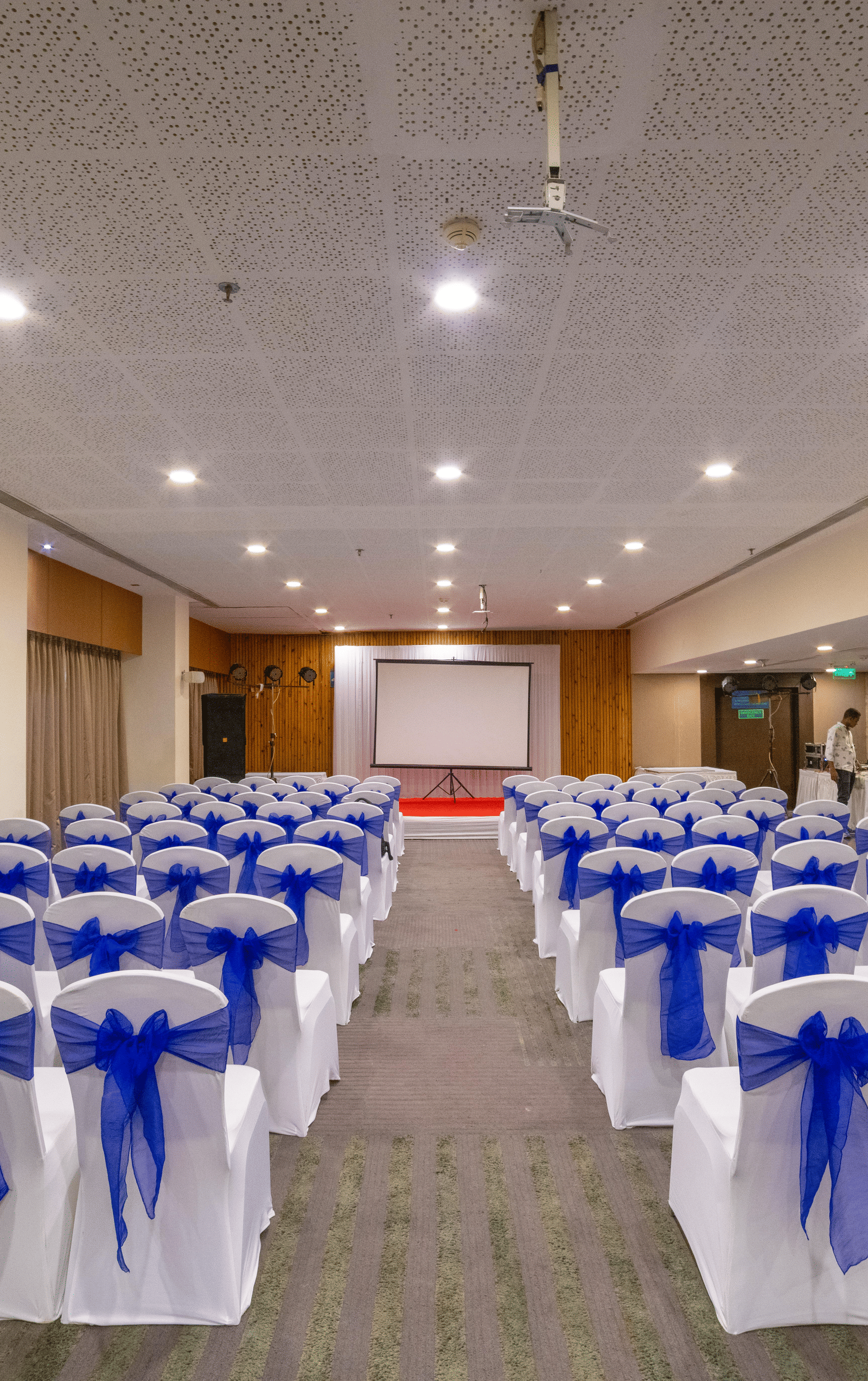 Back view of a banquet setup with rows of white chairs adorned with blue sashes - Narayani Heights Hotel & Resorts
