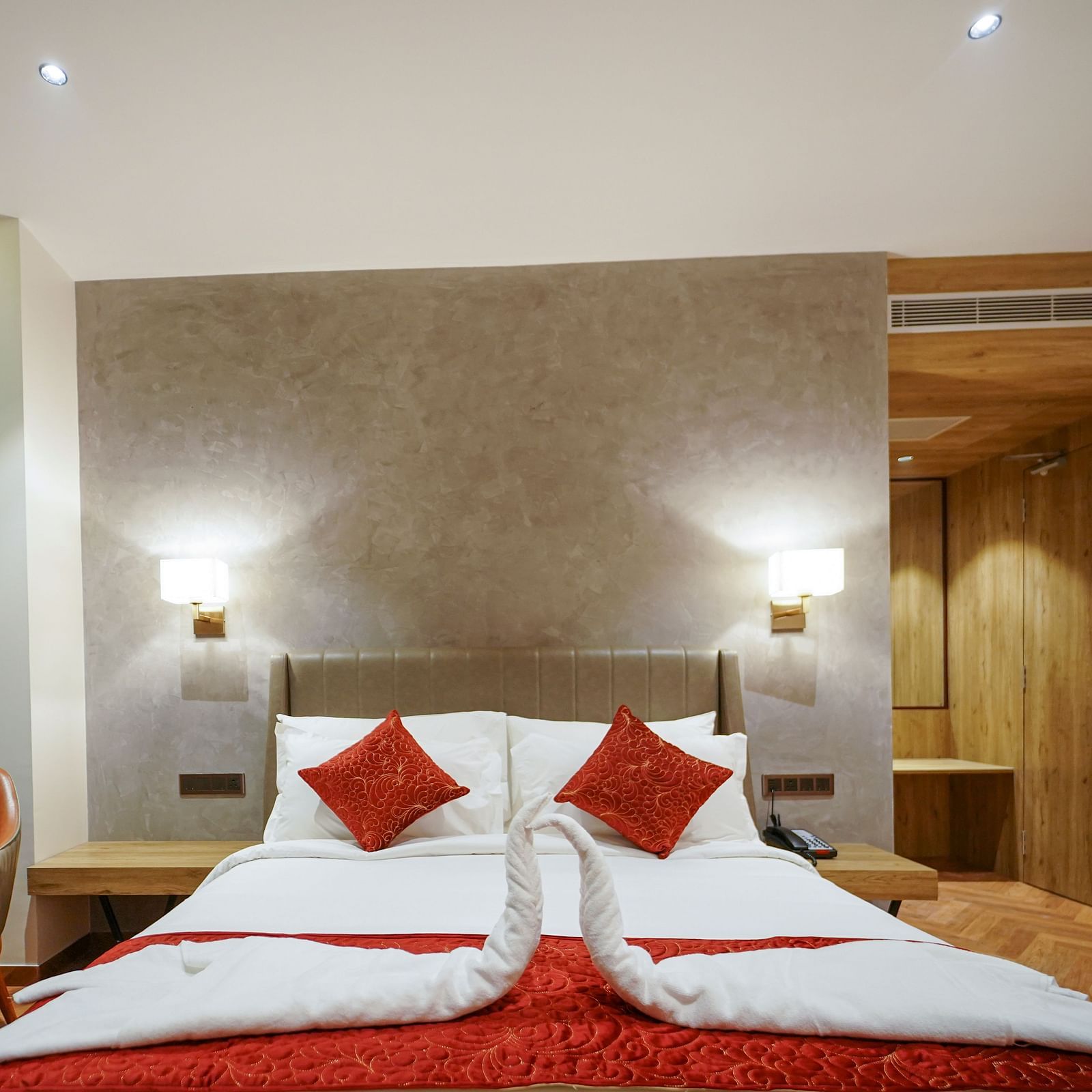 A hotel room features a bed with decorative folded linens, pillows, bedside lamps, a chair, a small table with flowers, and curtains - Hotel Park Inn, Nellore.