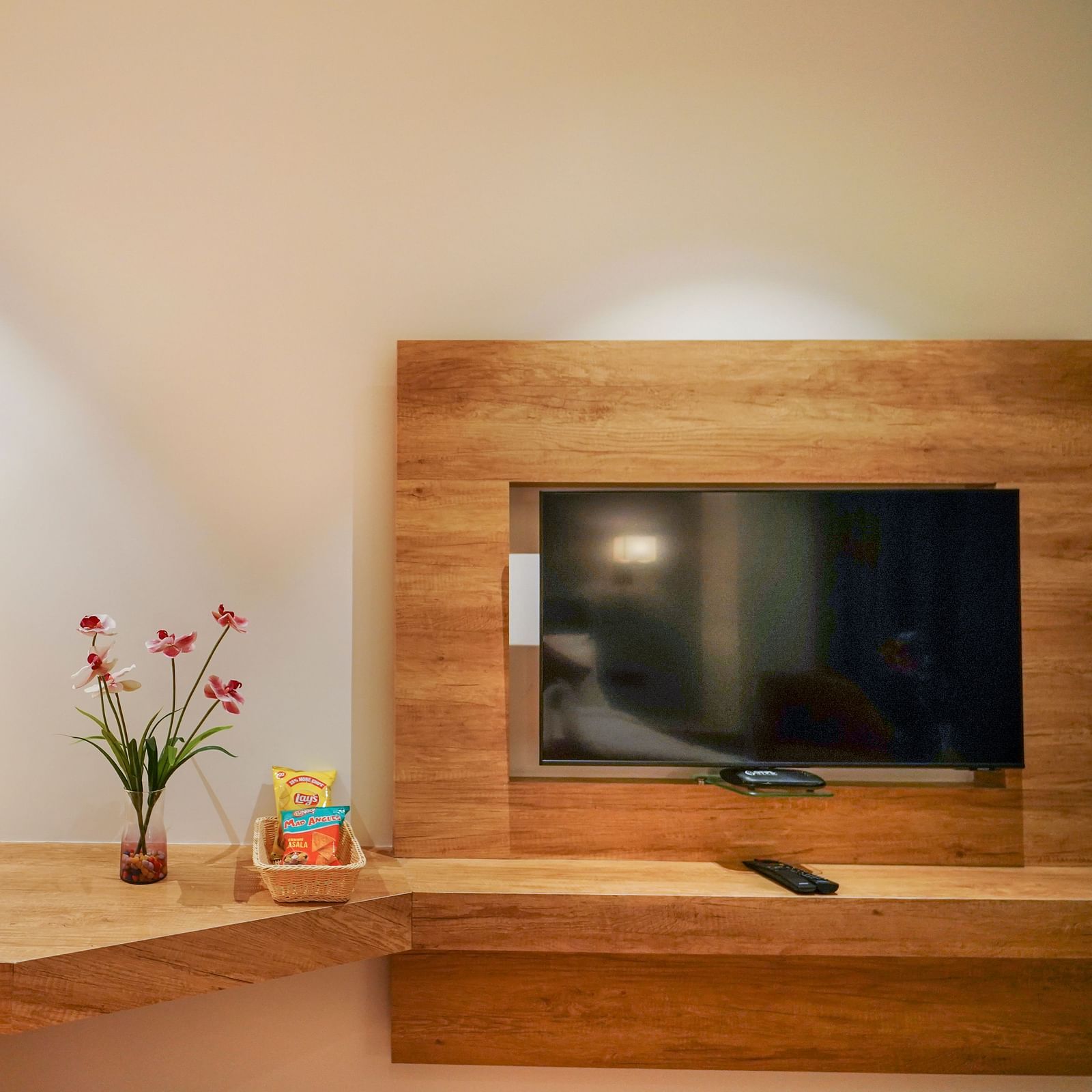 A section of a hotel room shows a desk with a lamp and flowers, a mounted television, and a chair partially visible - Hotel Park Inn, Nellore.