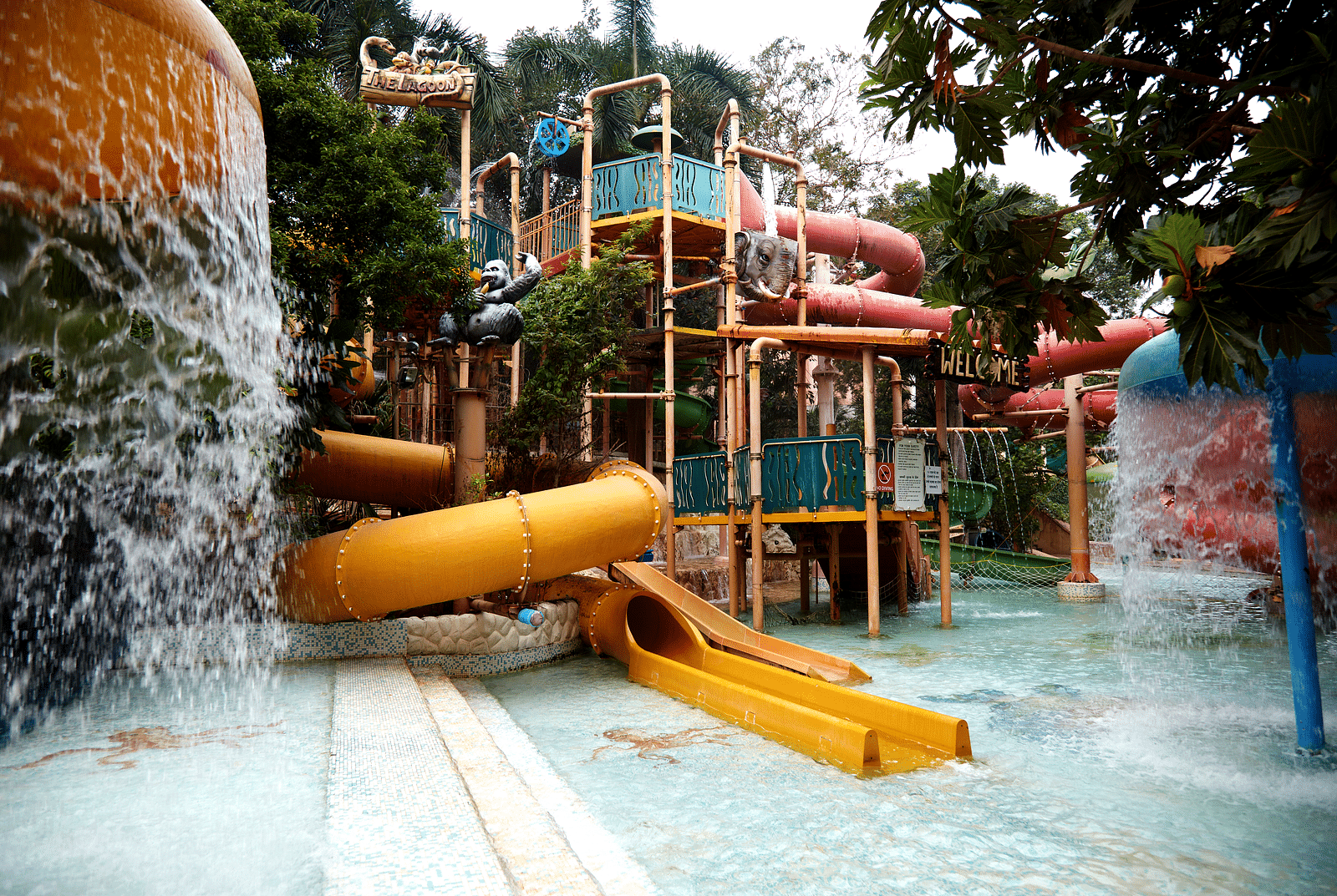 A vibrant scene at Water Kingdom in Mumbai, showcasing a yellow water slide, Lagoon and various water play structures.