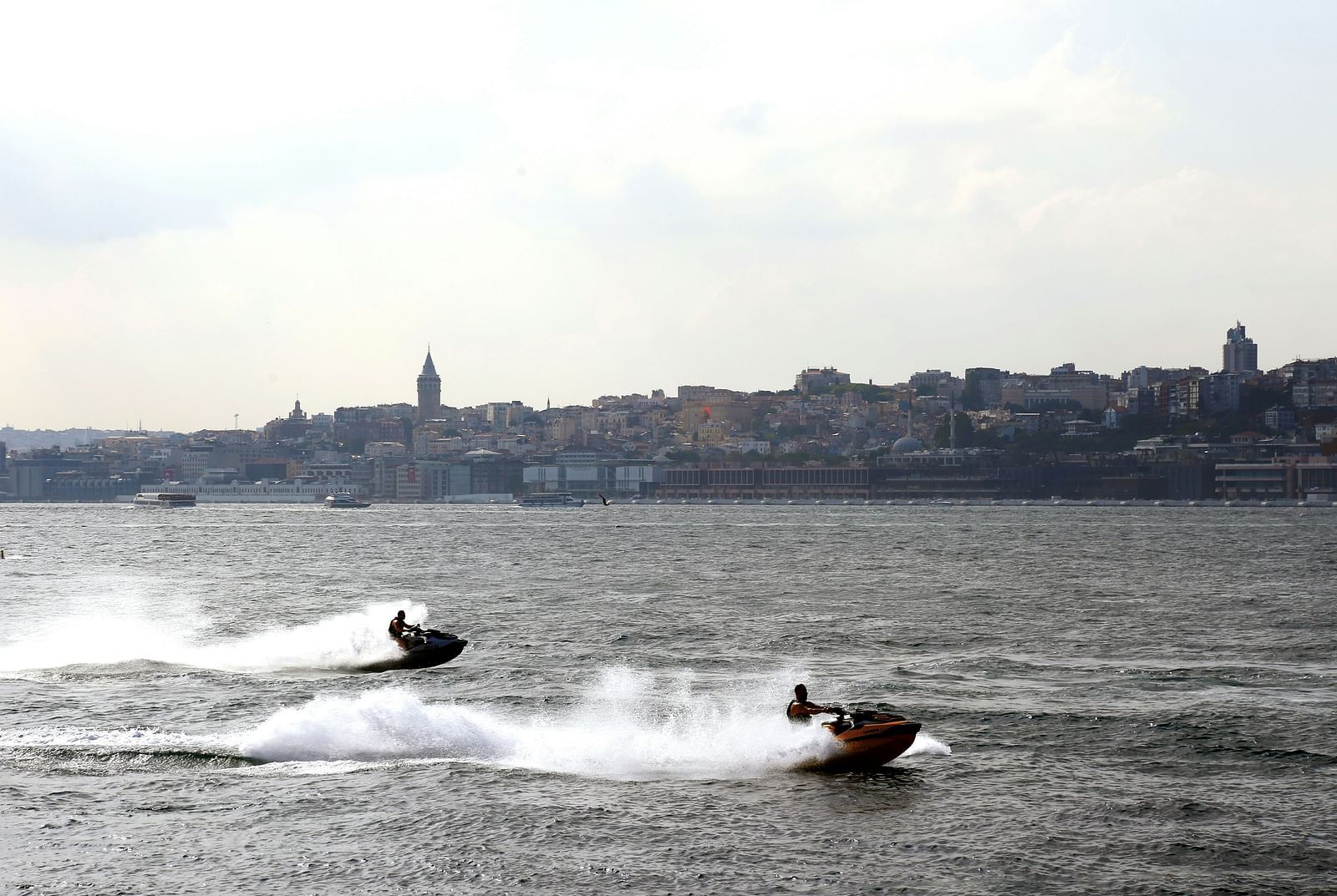 two people jet skiing on the water with a city skyline in the background.