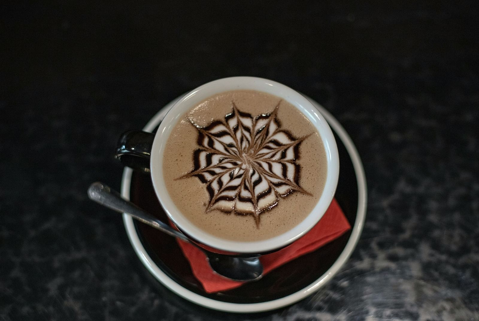 An aerial view of a cup of coffee kept on a saucer with a tissue below it.