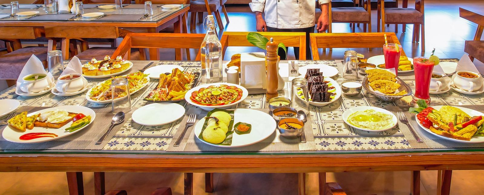 A chef stands near tables laden with food in a dining area at Vedikant Resorts The Mallard Corbett.