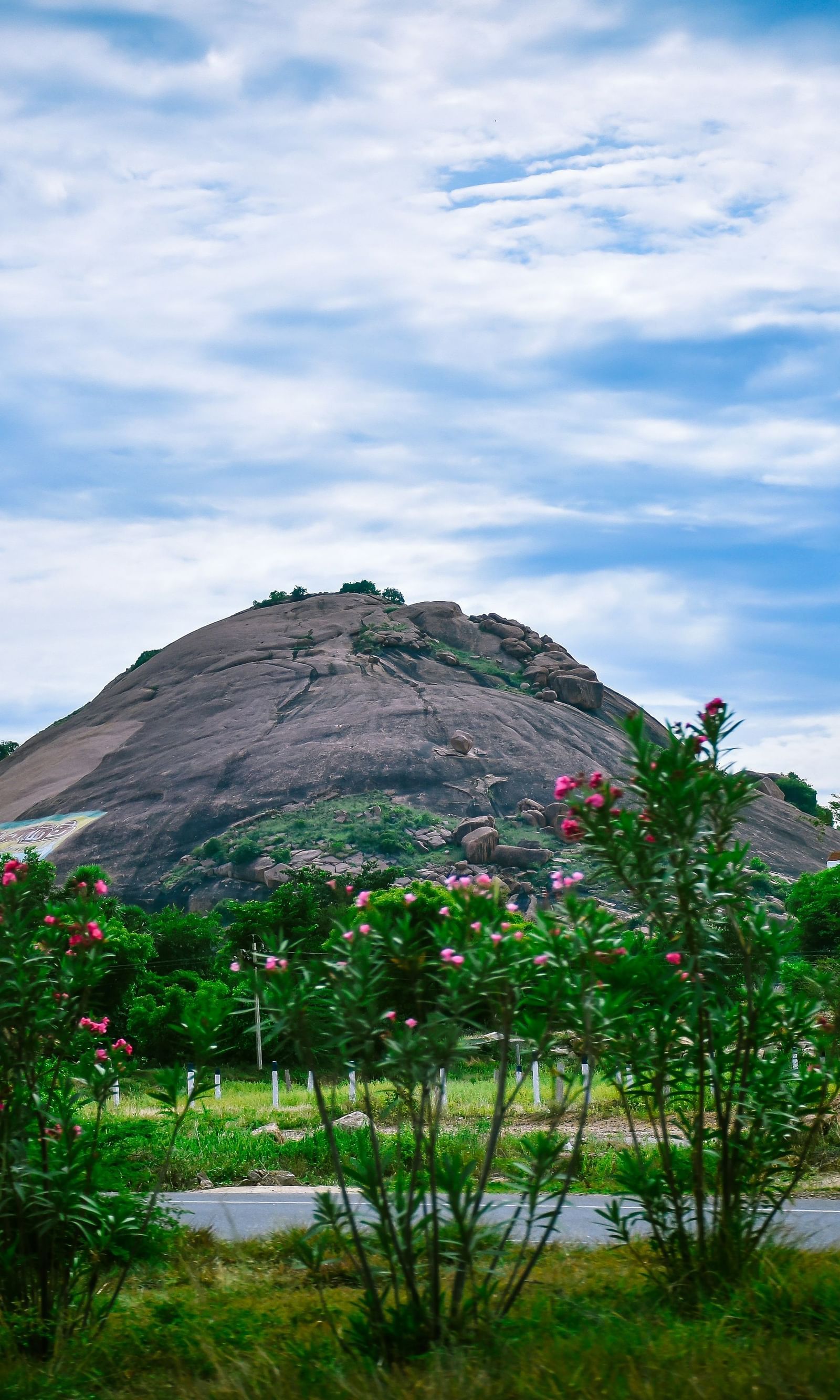 A scenic hill rises beyond a green field, under a sky filled with gentle blue hues - Grand Madurai by GRT Hotels