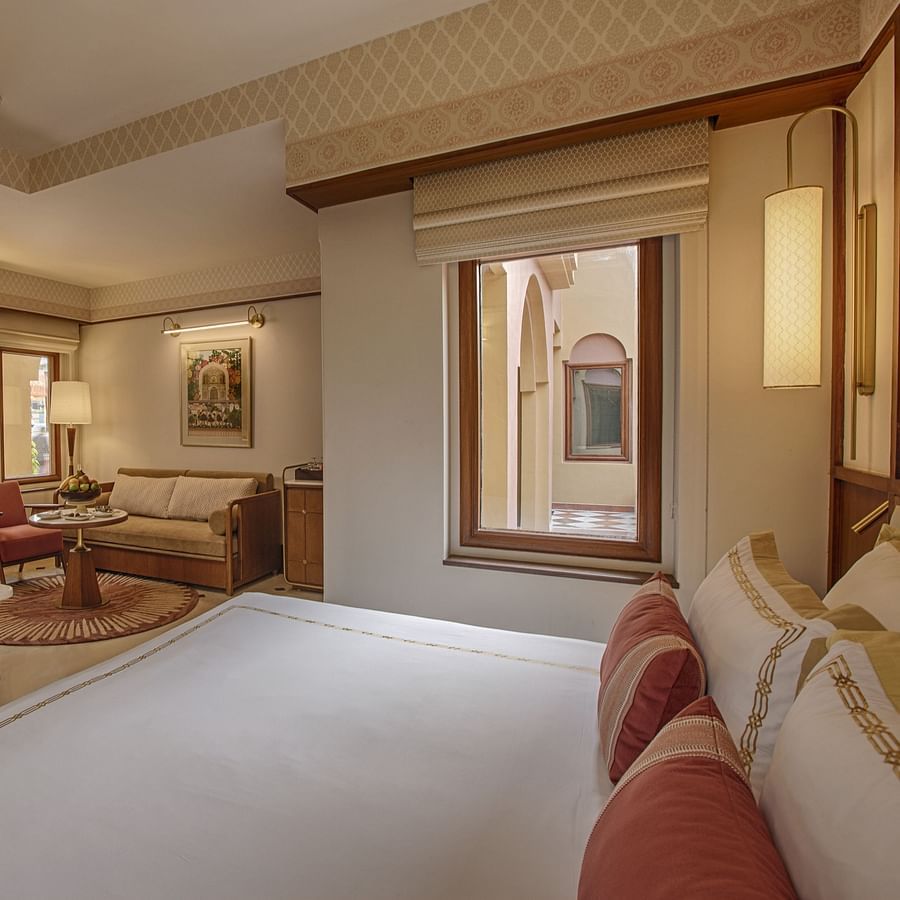 A hotel bedroom with a neat bed, wall-mounted TV, small window, and a seating area with a sofa, chair, and coffee table - Heritage Village Resorts & Spa, Manesar