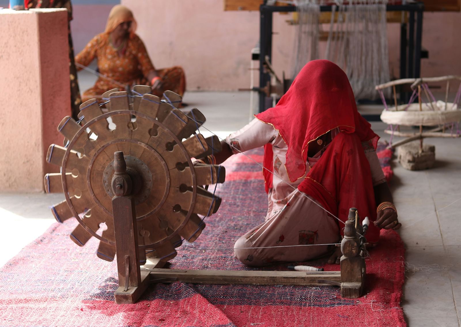 A view of a woman using a spinning wheel while wearing a red cloth over her head.