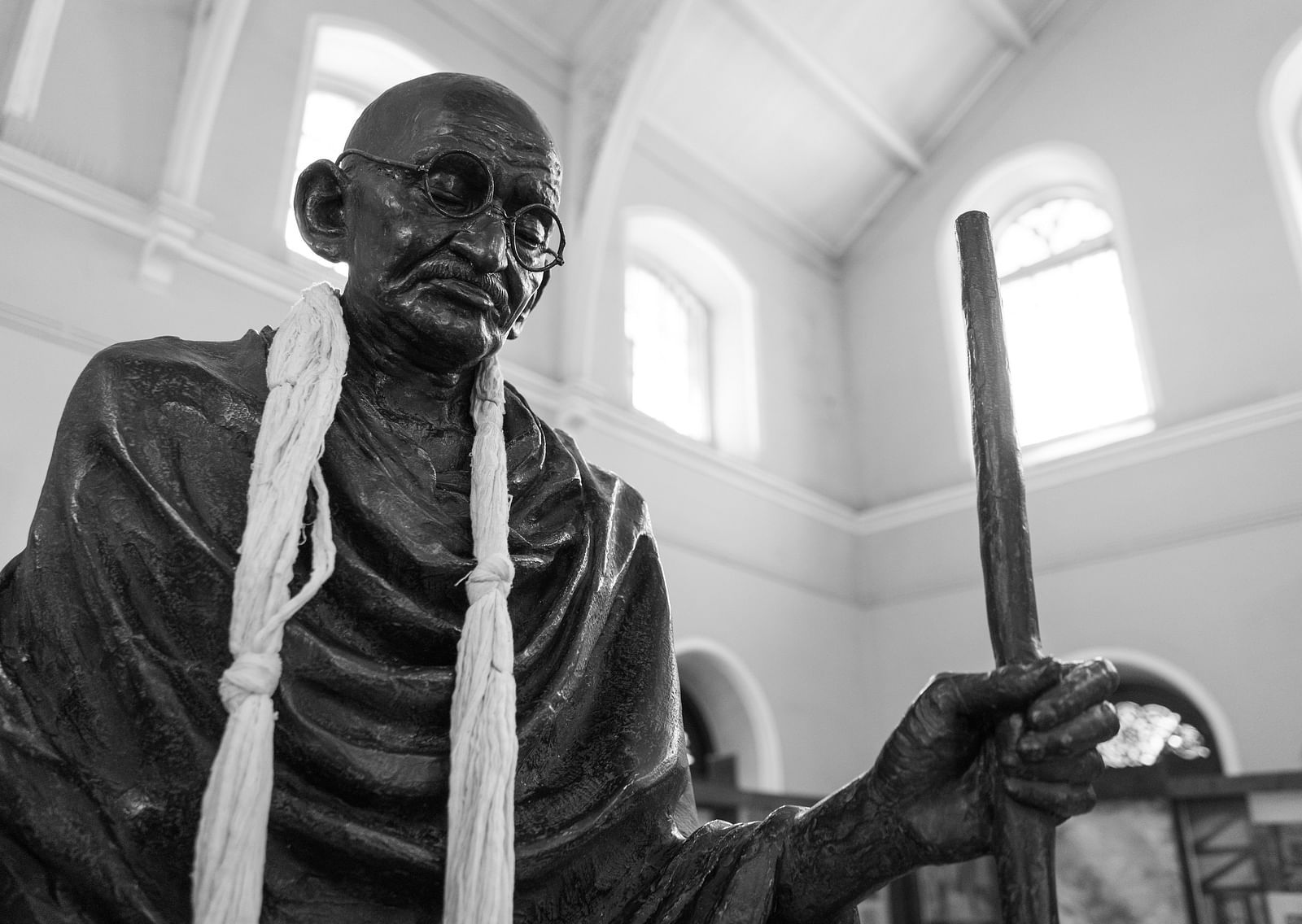 A close up of a statue of Mahathma Gandhi inside Aga Khan Palace with windows in the background.