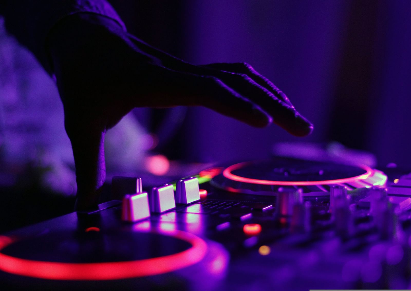 A close up shot of a DJ using his turntable with neon lights to mix music.