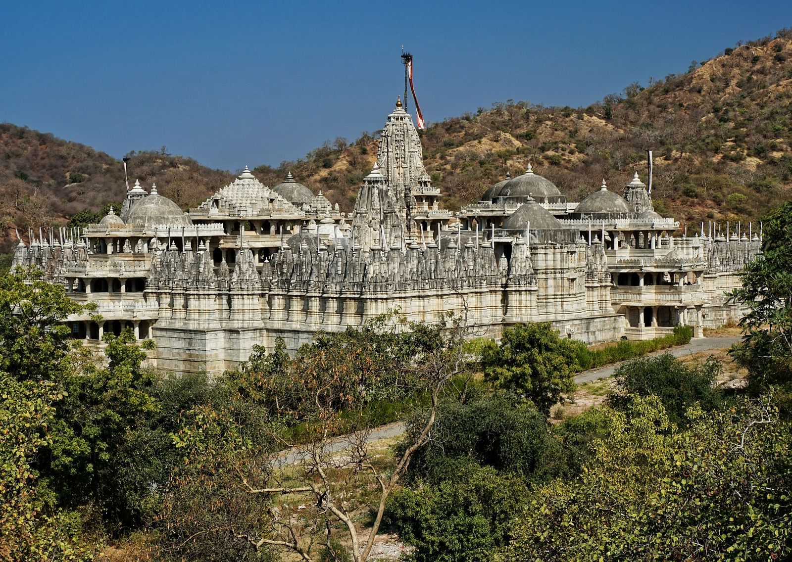 An far out view of a jain temple with white exterior in the centre with hills in the background.