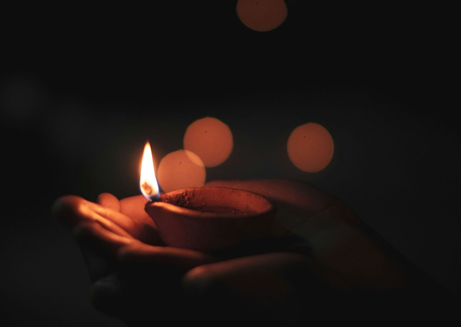 A close up of a person holding a lit diya in their hand with the background blurred.