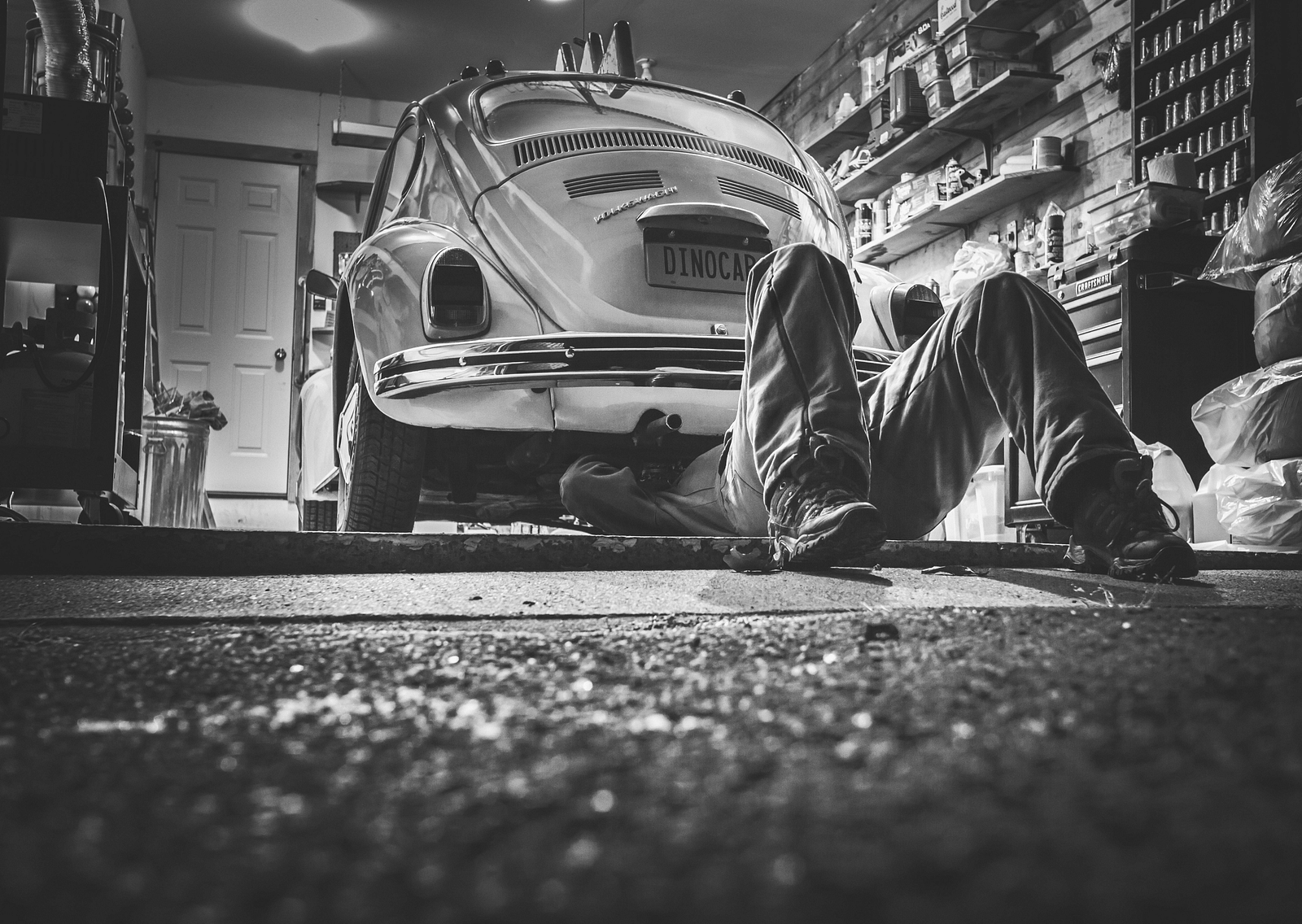 A black and white image of a person working on a car in a garage.