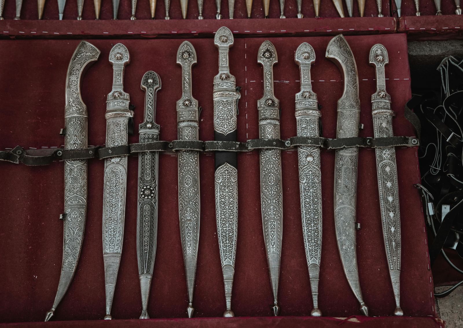 A close-up shot of highly decorative, silver-inlaid daggers or ceremonial knives, displayed side-by-side.