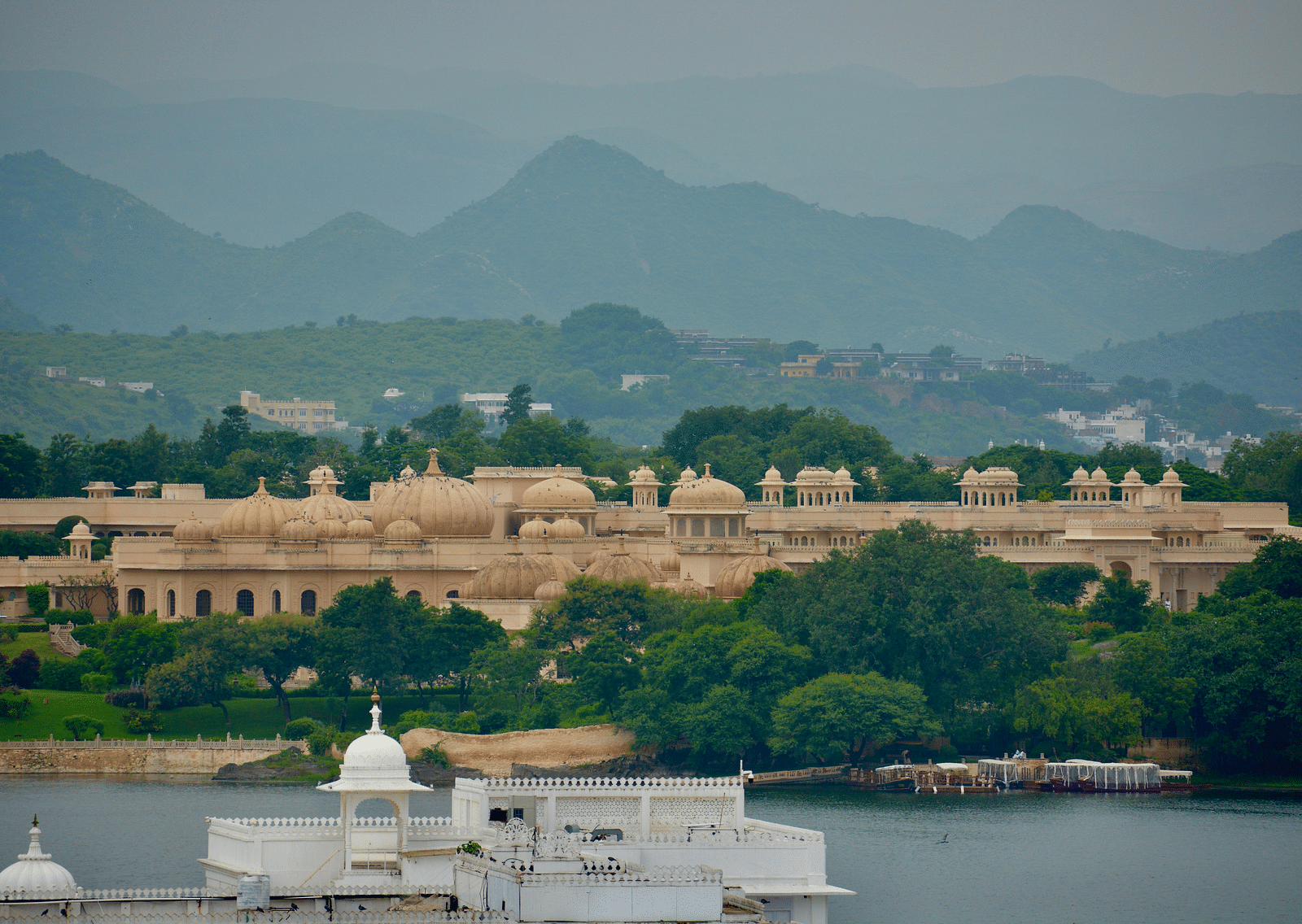 An overview of City palace seen around green trees with aravali hills in the background.
