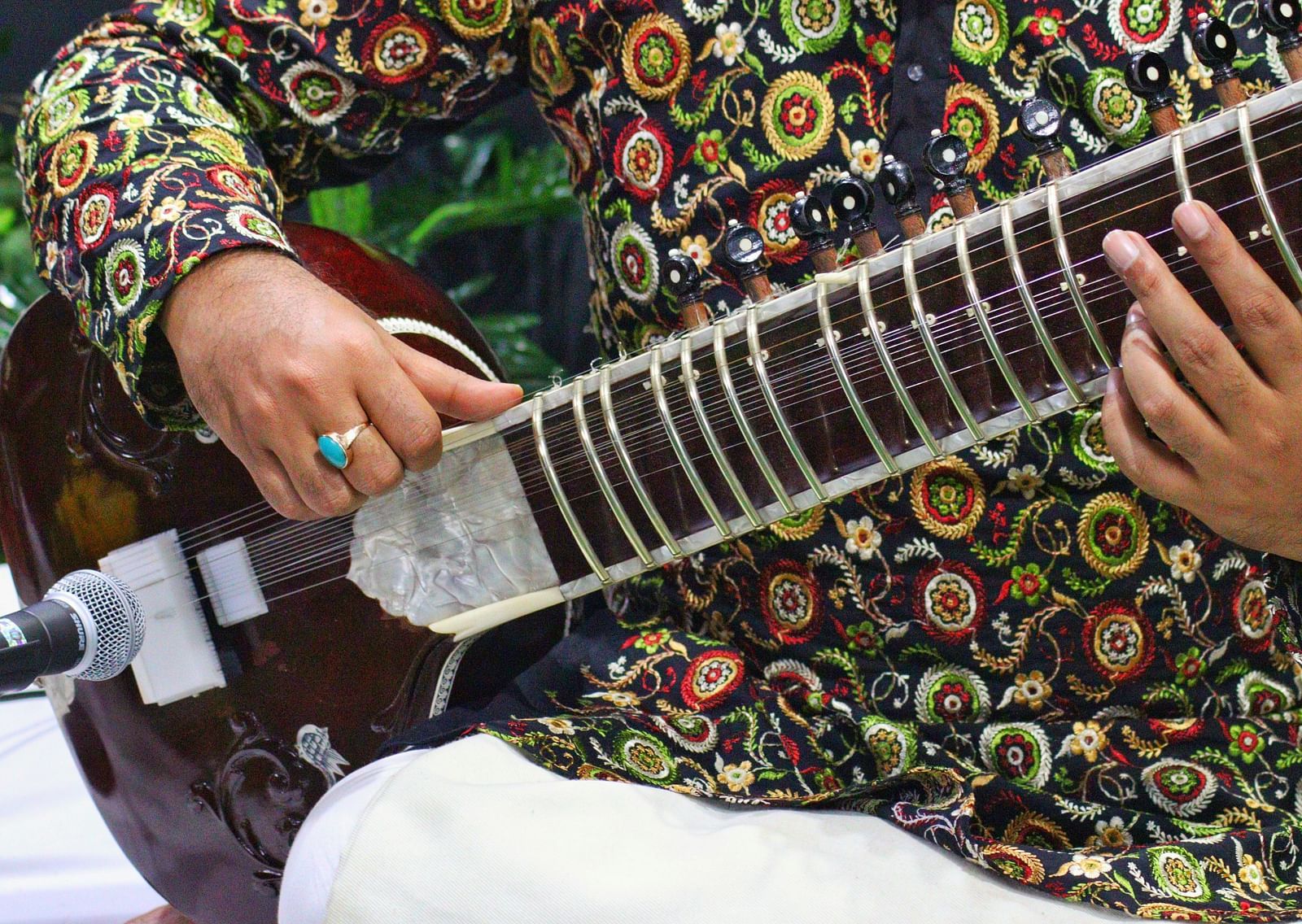 A close up of a person using a sitar while being seating with a mic near the sitar.