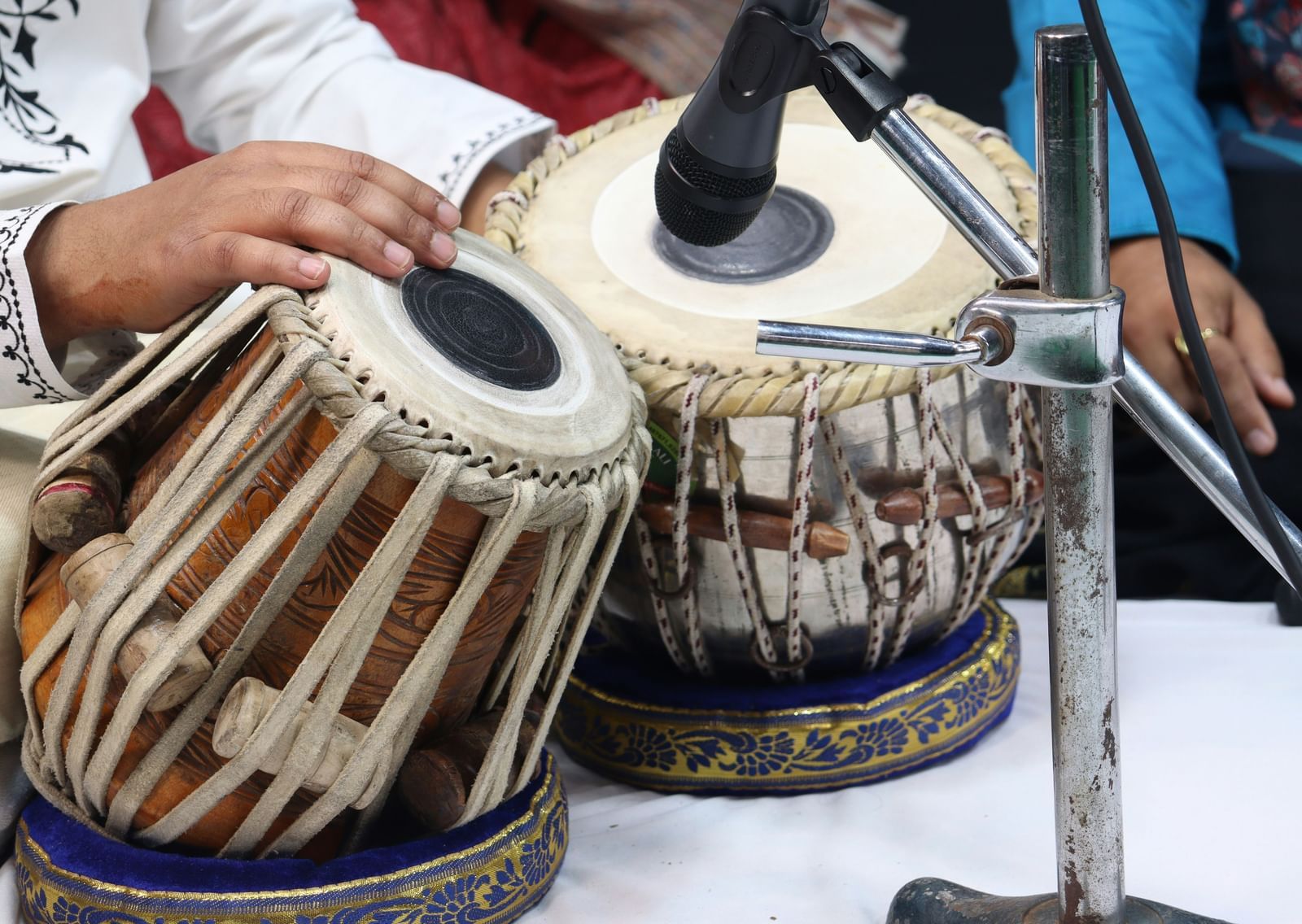 A close-up shot of a person's hands playing a pair of tablas, with intricate patterns on the instruments.