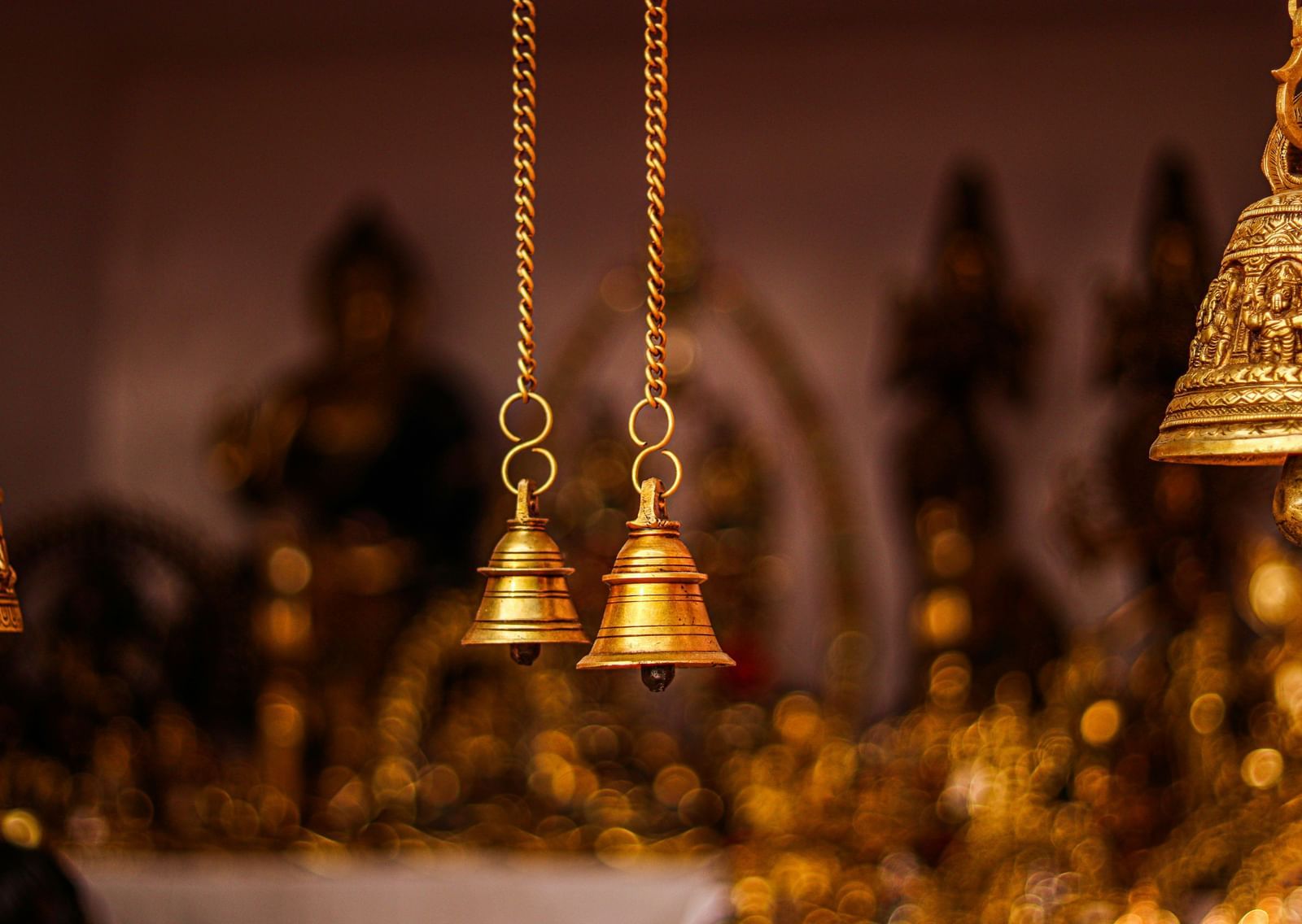 Bells hanging on small chains, with a blurred background of idols.