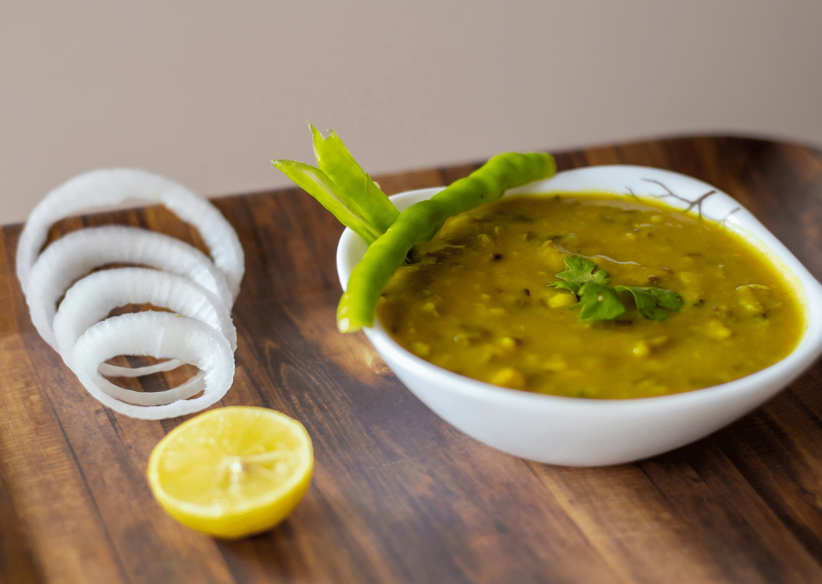 An overview of a dal dish kept in a bowl with sliced raw onion rings and a slice of lemon next to it.