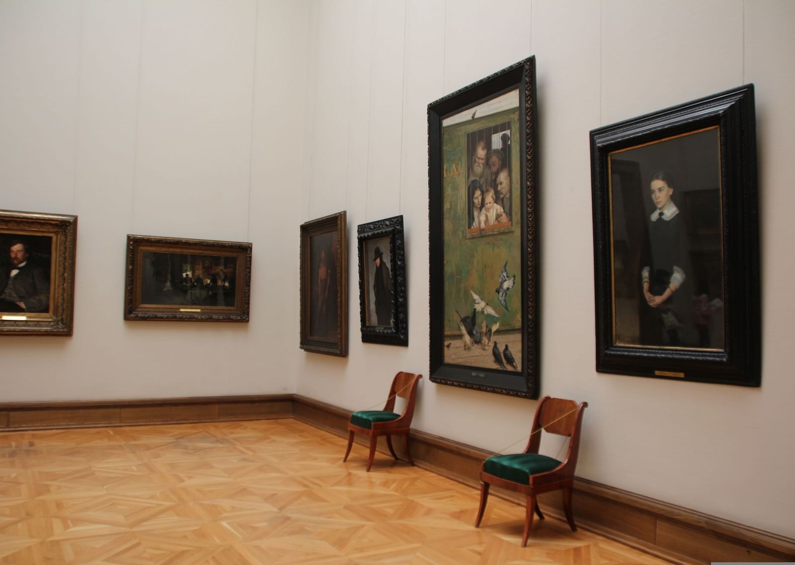 An overview of a museum with paintings hung on the wall and two chairs kept next to one of the painting.